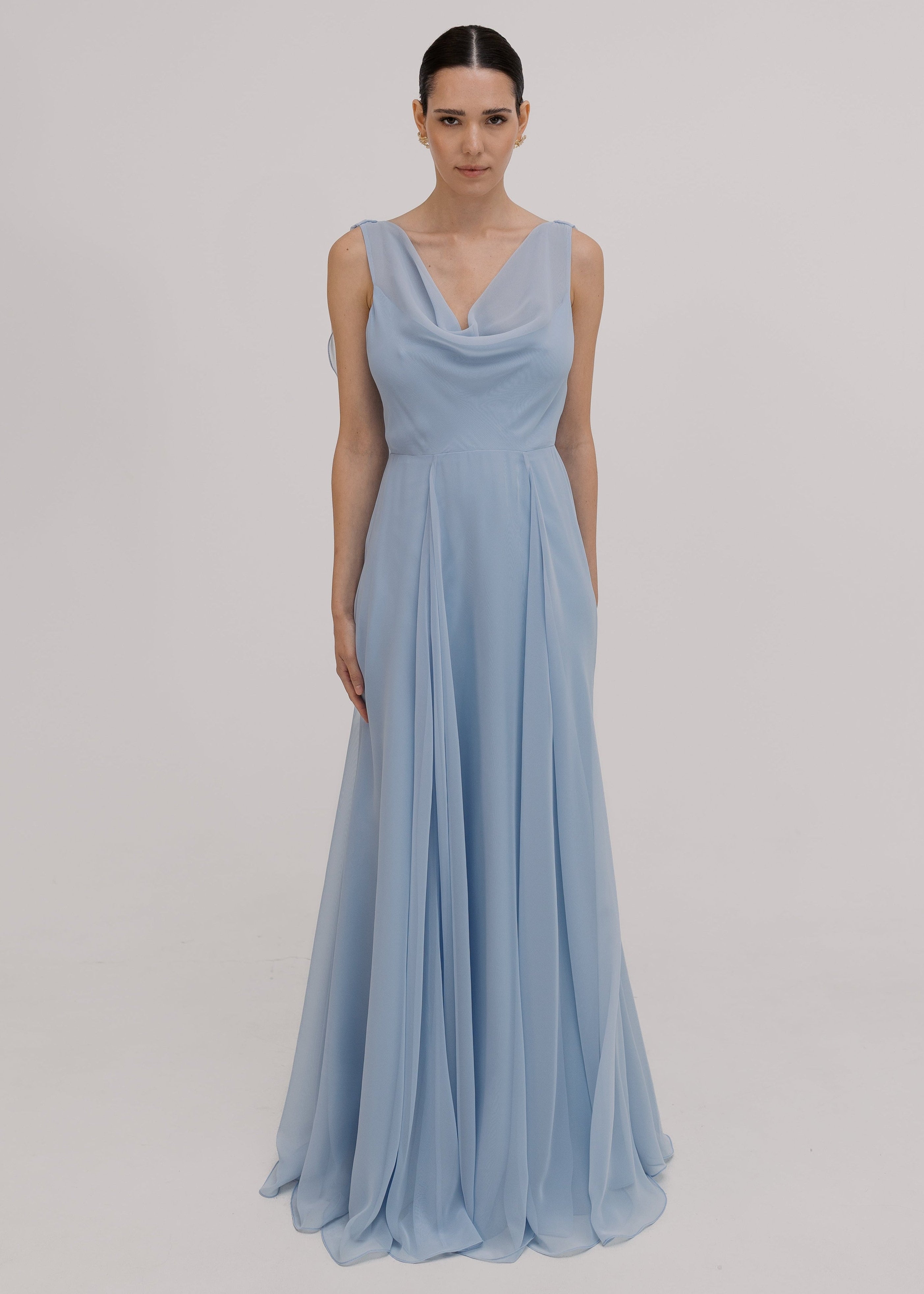 Model wearing a dusty blue bridesmaid dress in chiffon with cowl neckline and flowing chiffon skirt by TH&TH Bridesmaids.
