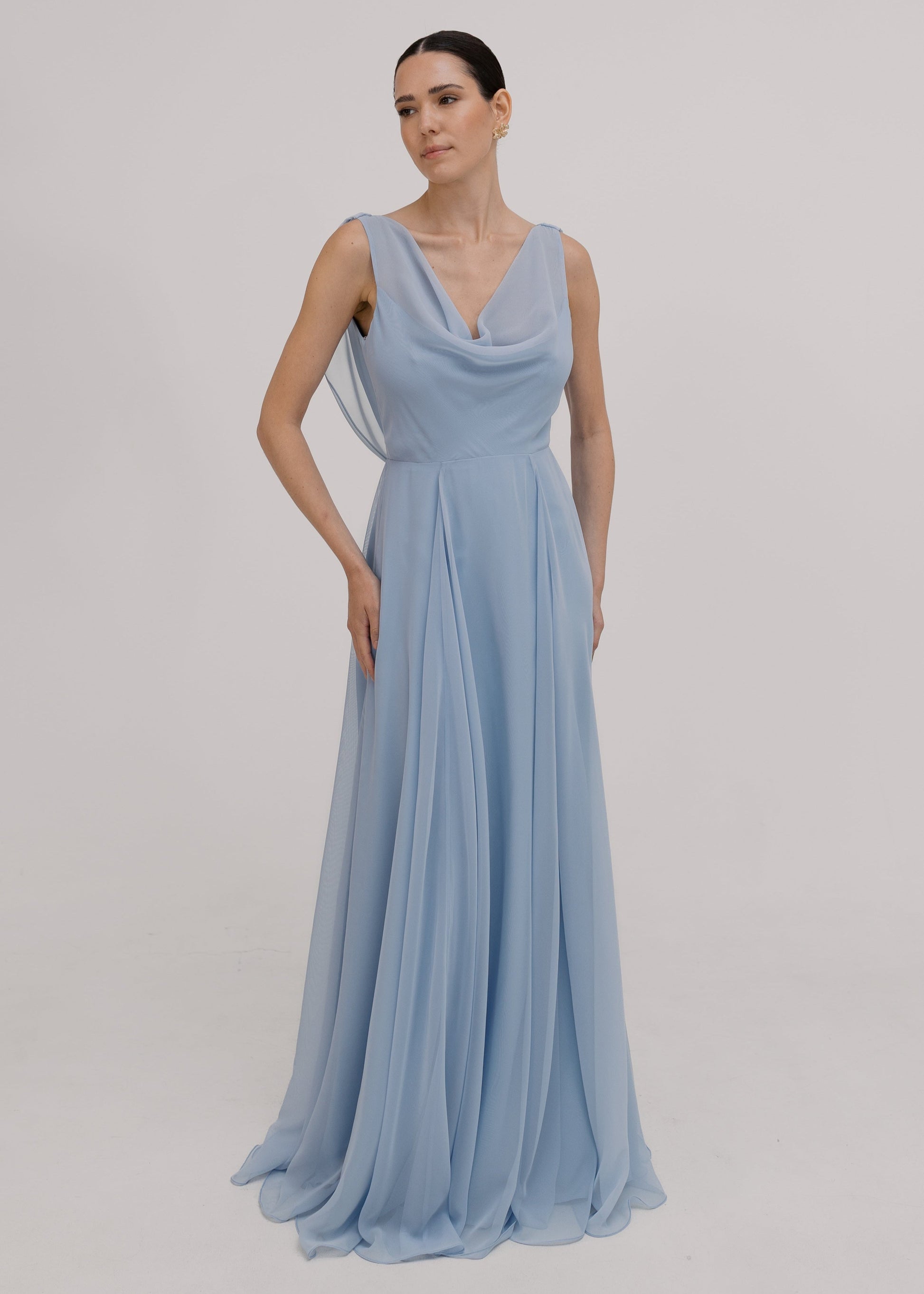 Model wearing a dusty blue bridesmaid dress in chiffon with cowl neckline and flowing chiffon skirt by TH&TH Bridesmaids.
