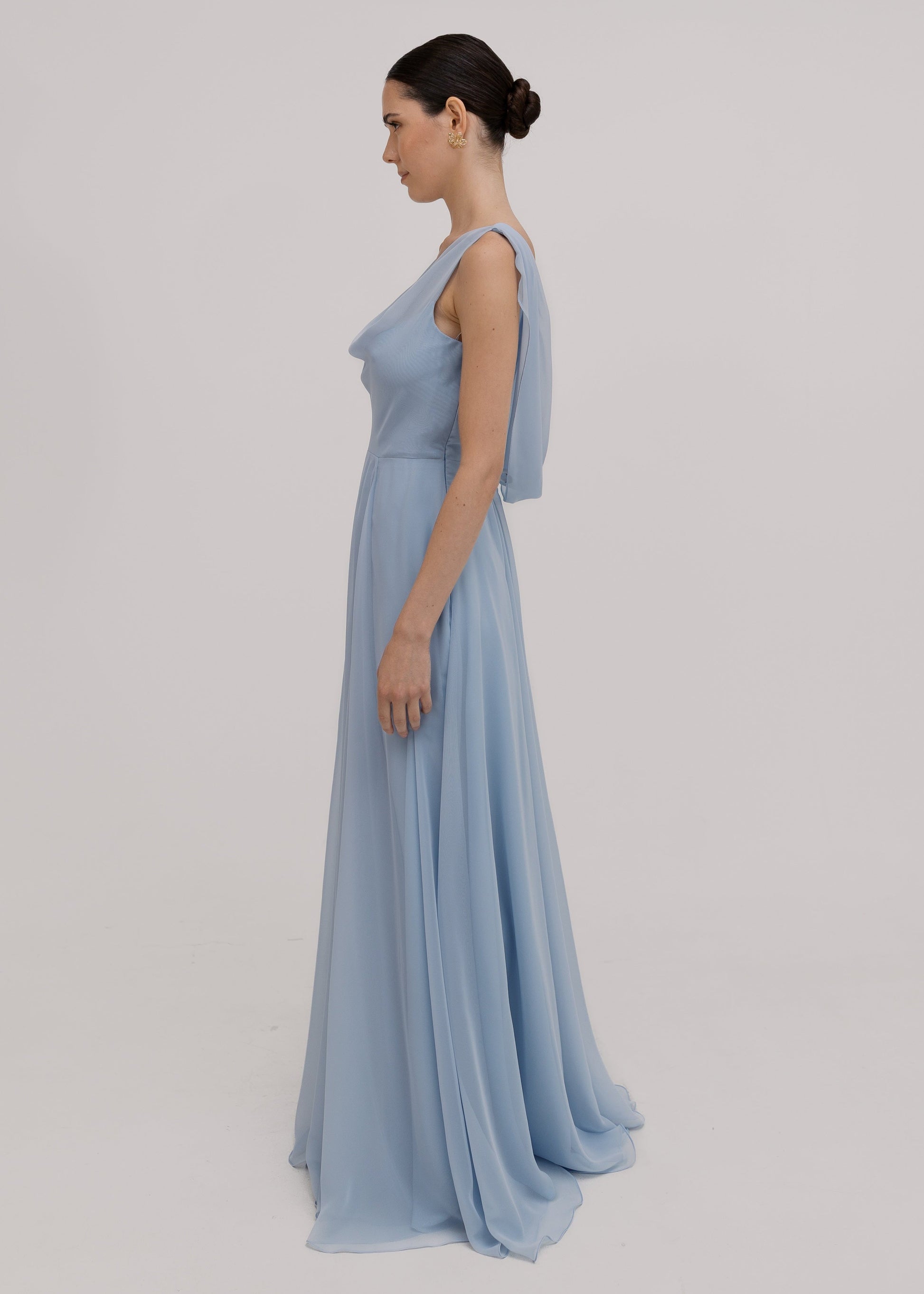 Model wearing a dusty blue bridesmaid dress in chiffon with cowl neckline and flowing chiffon skirt by TH&TH Bridesmaids.
