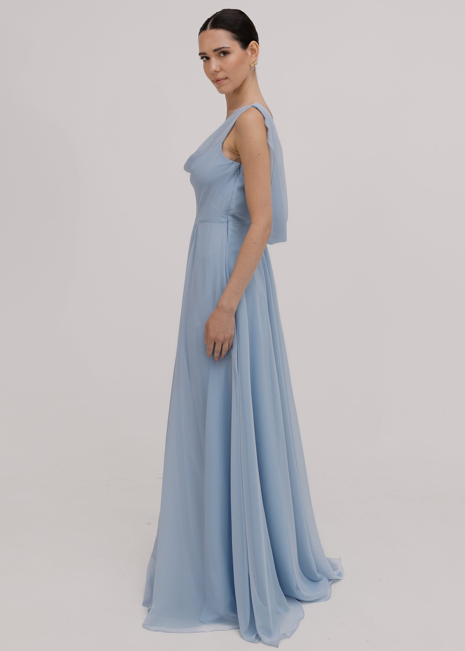 Model wearing a dusty blue bridesmaid dress in chiffon with cowl neckline and flowing chiffon skirt by TH&TH Bridesmaids.
