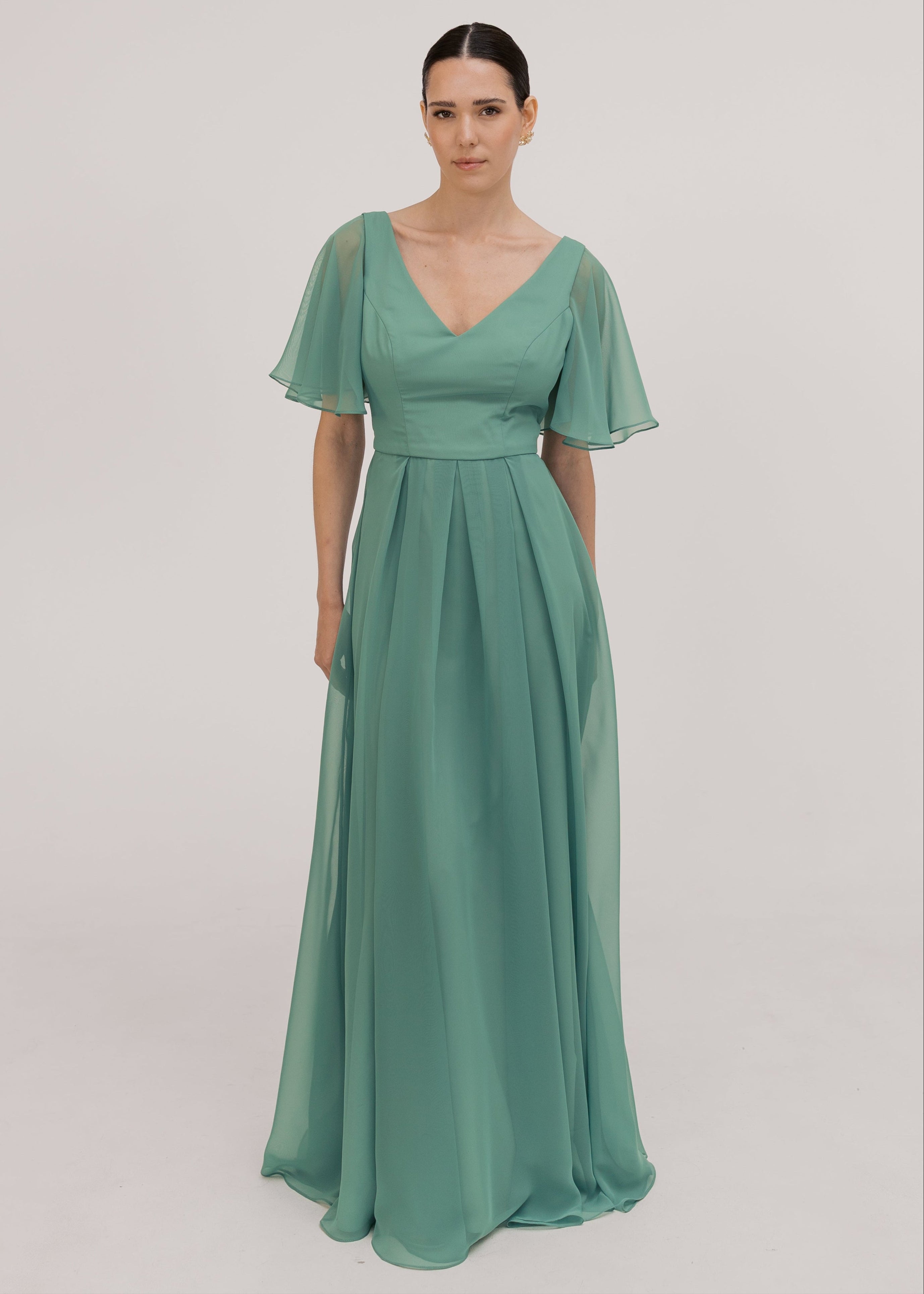 Model wears a sage green bridesmaid dress in chiffon with v front neckline, flutter sleeves and flowing chiffon skirt by TH&TH Bridesmaids. 