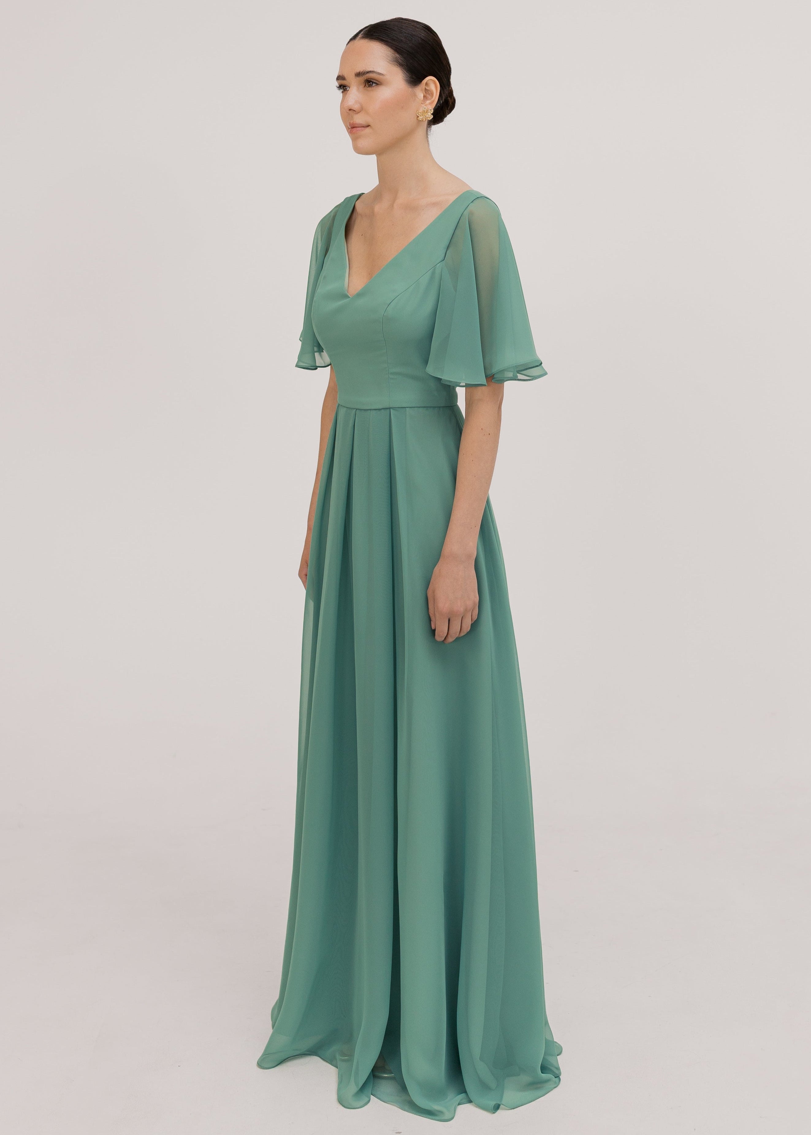Model wears a sage green bridesmaid dress in chiffon with v front neckline, flutter sleeves and flowing chiffon skirt by TH&TH Bridesmaids. 
