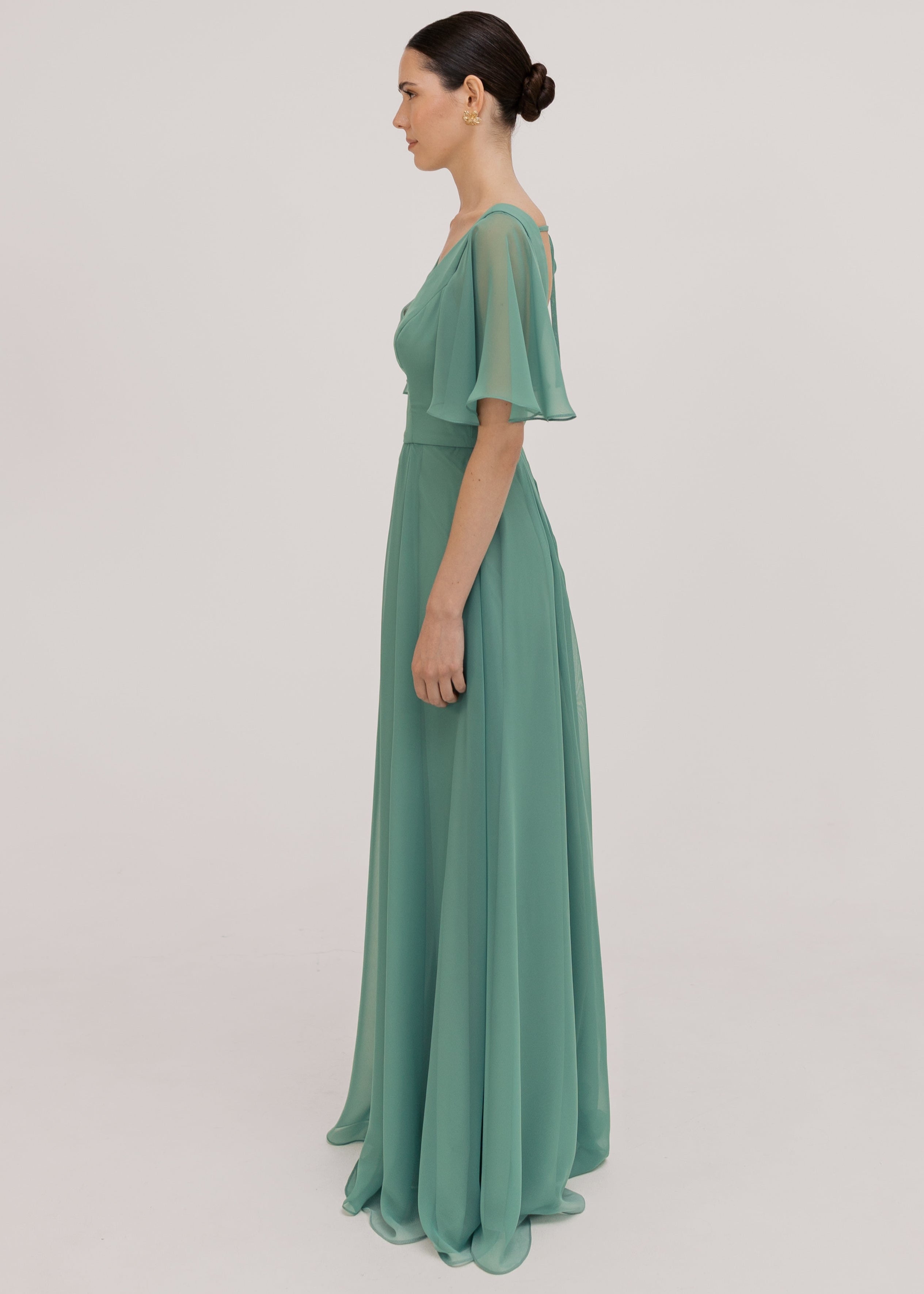 Model wears a sage green bridesmaid dress in chiffon with v front neckline, flutter sleeves and flowing chiffon skirt by TH&TH Bridesmaids. 
