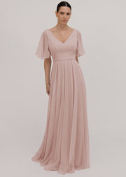 Model wears a blush pink bridesmaid dress in chiffon with v front neckline, flutter sleeves and flowing chiffon skirt by TH&TH Bridesmaids. 

