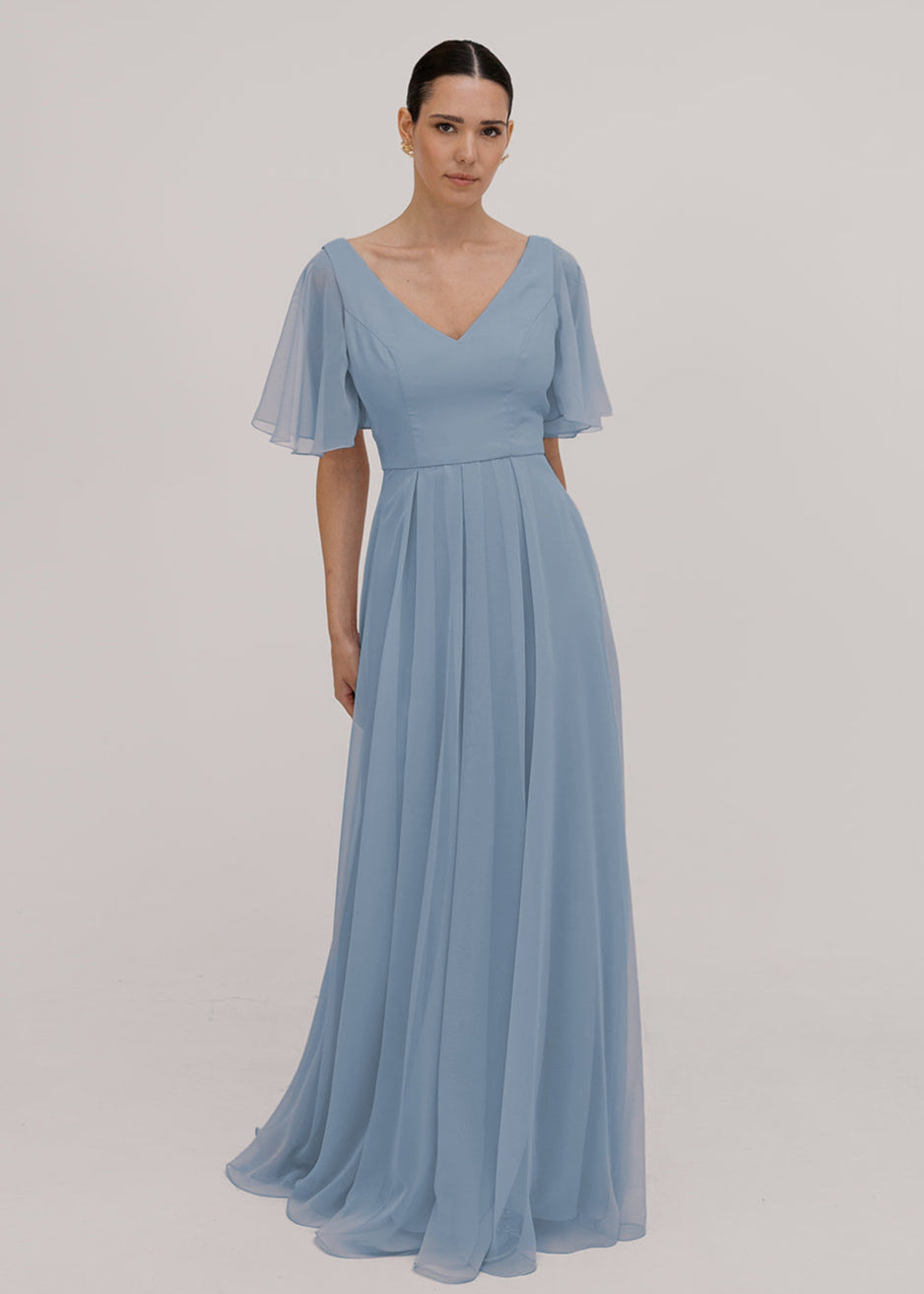 Model wears a dusty blue bridesmaid dress in chiffon with v front neckline, flutter sleeves and flowing chiffon skirt by TH&TH Bridesmaids. 

