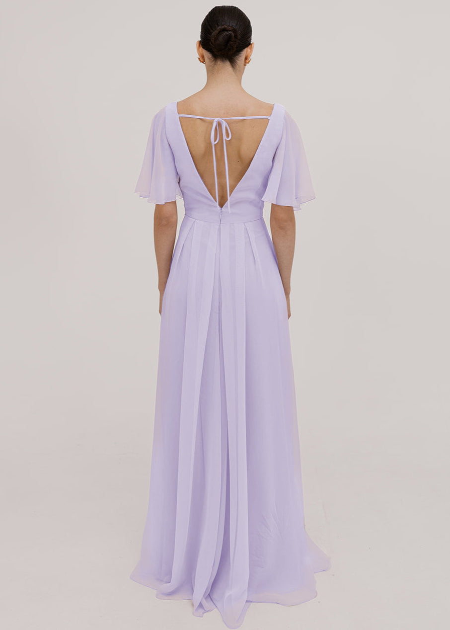 Model wears a lilac bridesmaid dress in chiffon with low open back detail, flutter sleeves and flowing chiffon skirt by TH&TH Bridesmaids. 