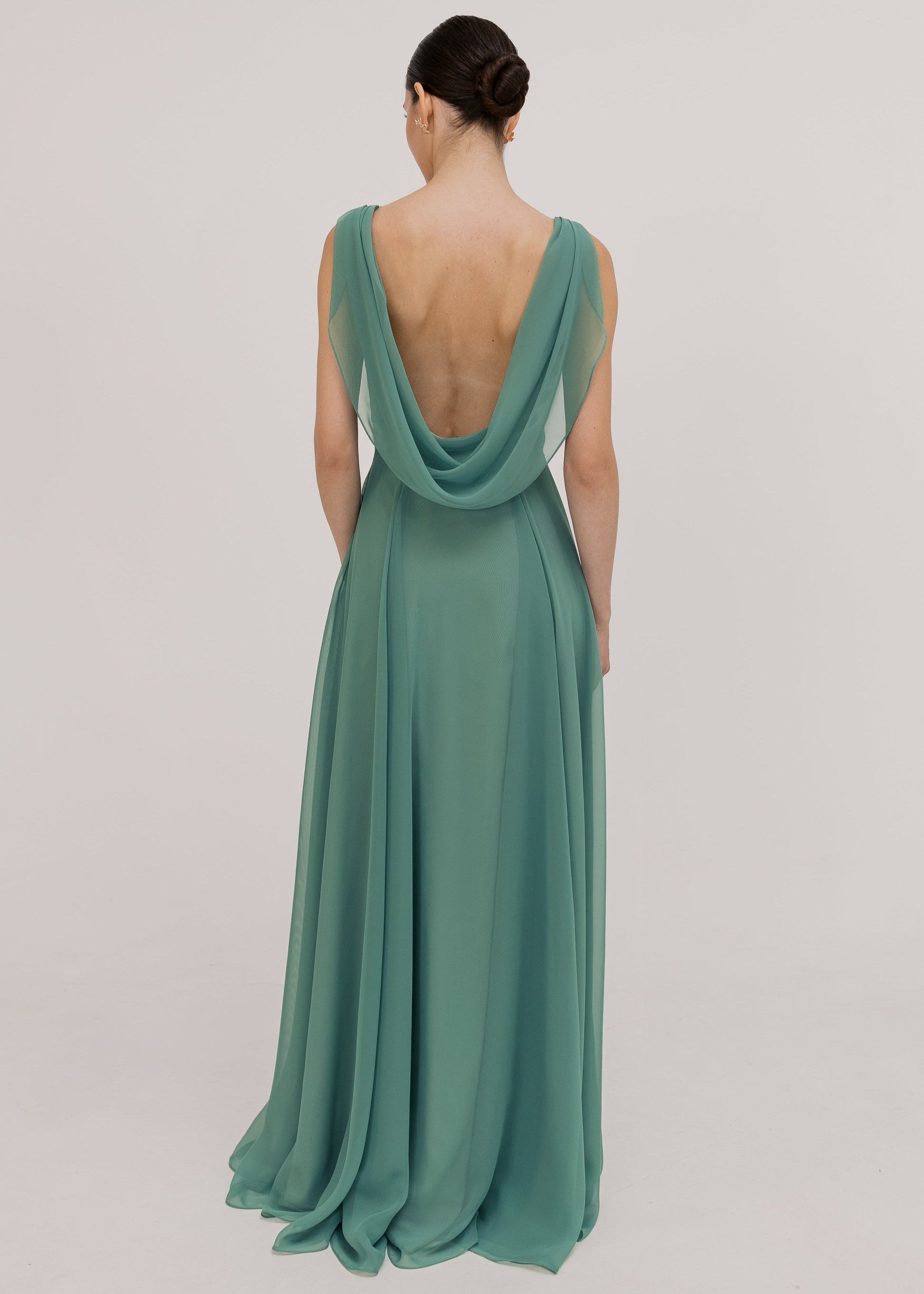 Model wearing a sage green bridesmaid dress with v low cowl back detail and flowing chiffon skirt by TH&TH Bridesmaids.