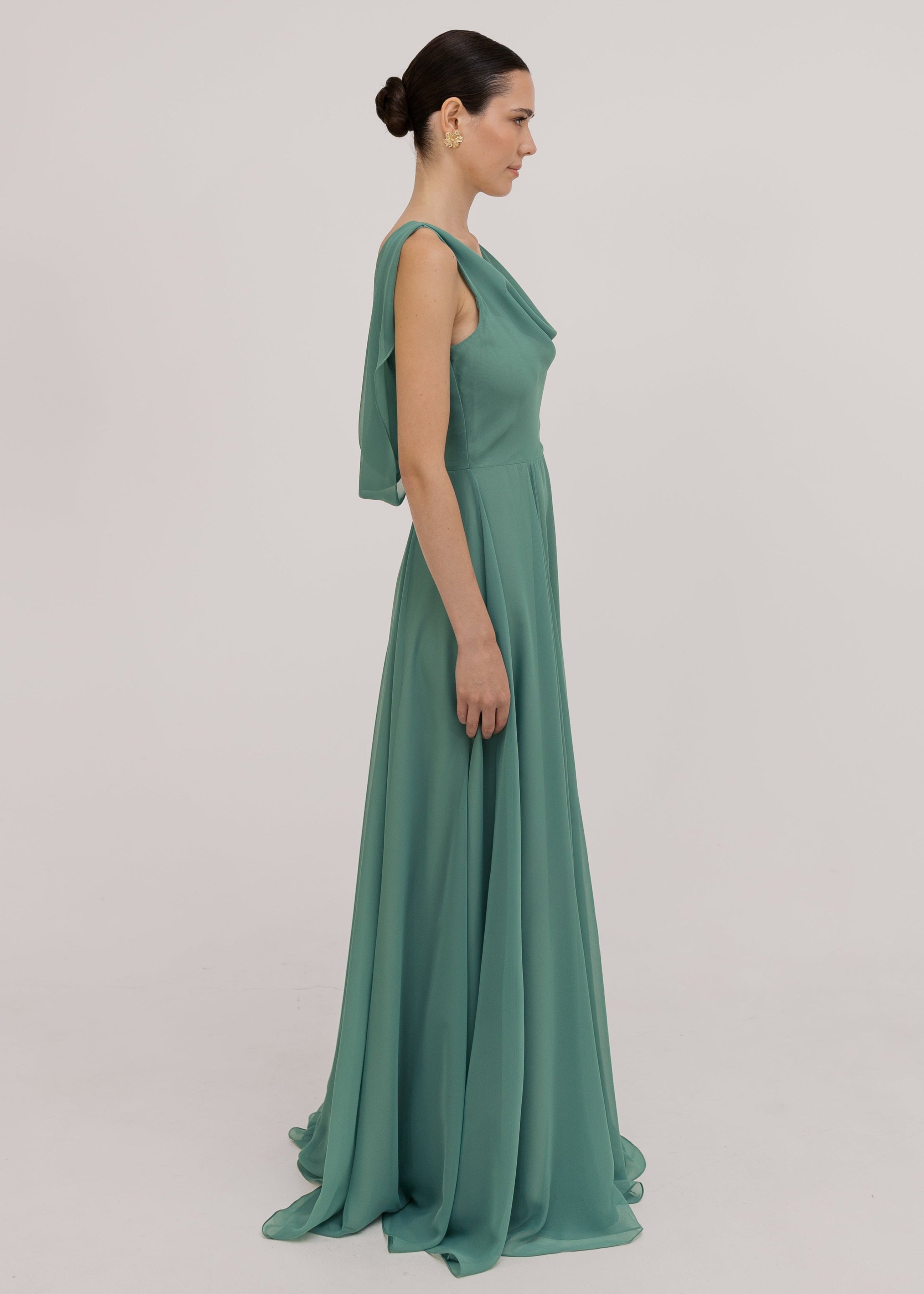 Model wearing a sage green bridesmaid dress with cowl neckline and flowing chiffon skirt side view by TH&TH Bridesmaids.