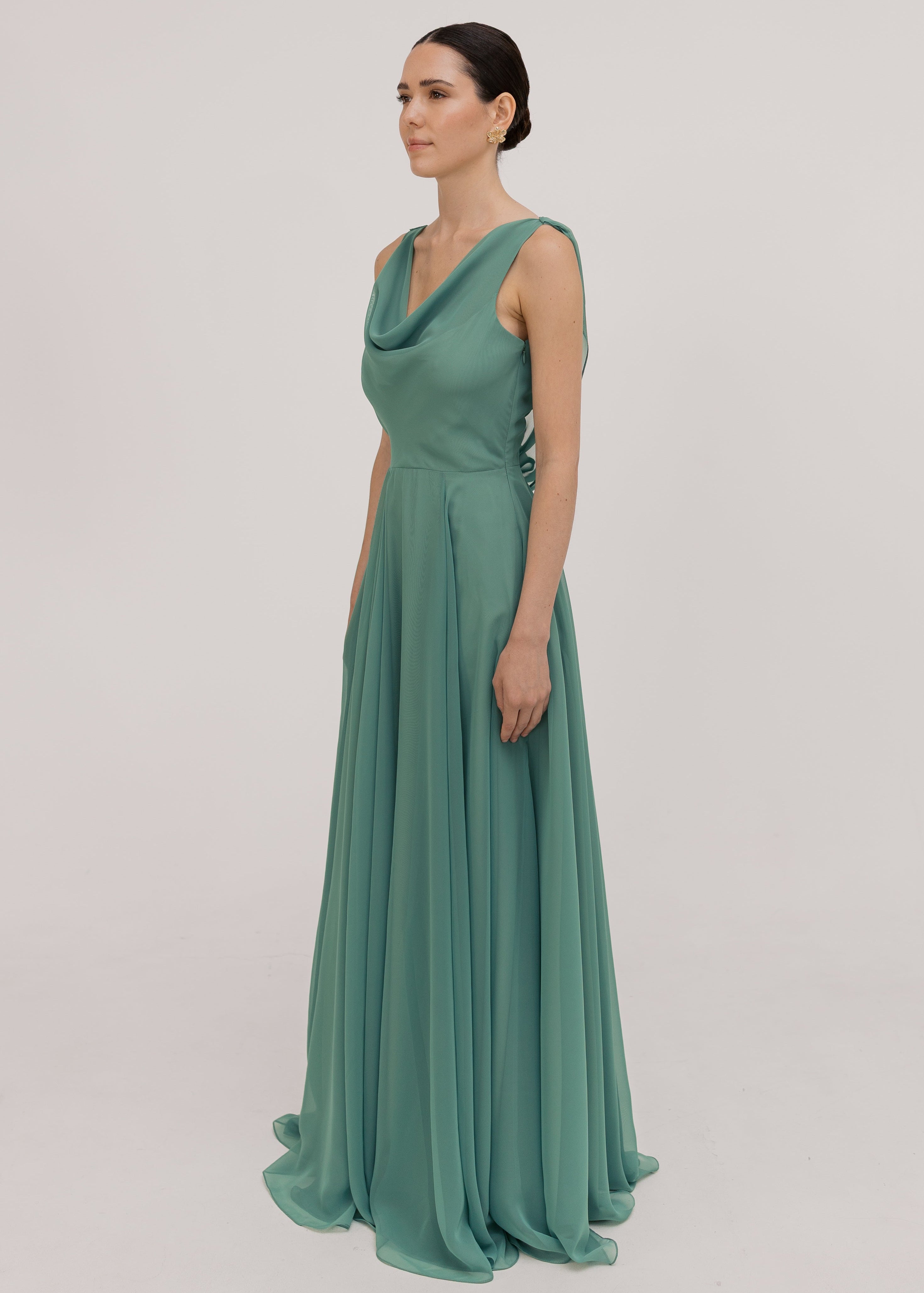 Model wearing a sage green bridesmaid dress with cowl neckline and flowing chiffon skirt side view by TH&TH Bridesmaids.