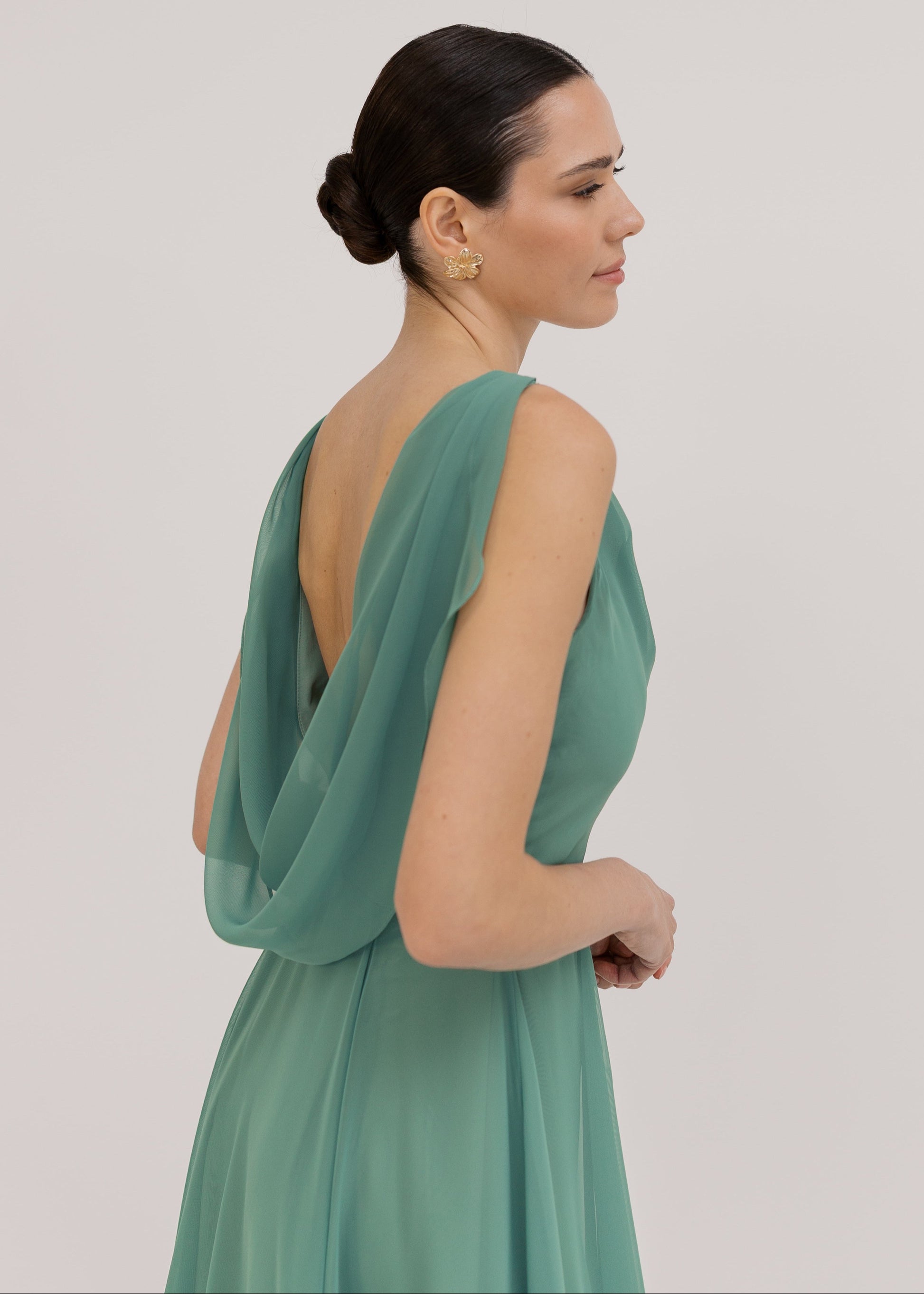 Model wearing a sage green bridesmaid dress with low cowl back detail and flowing chiffon skirt by TH&TH Bridesmaids.