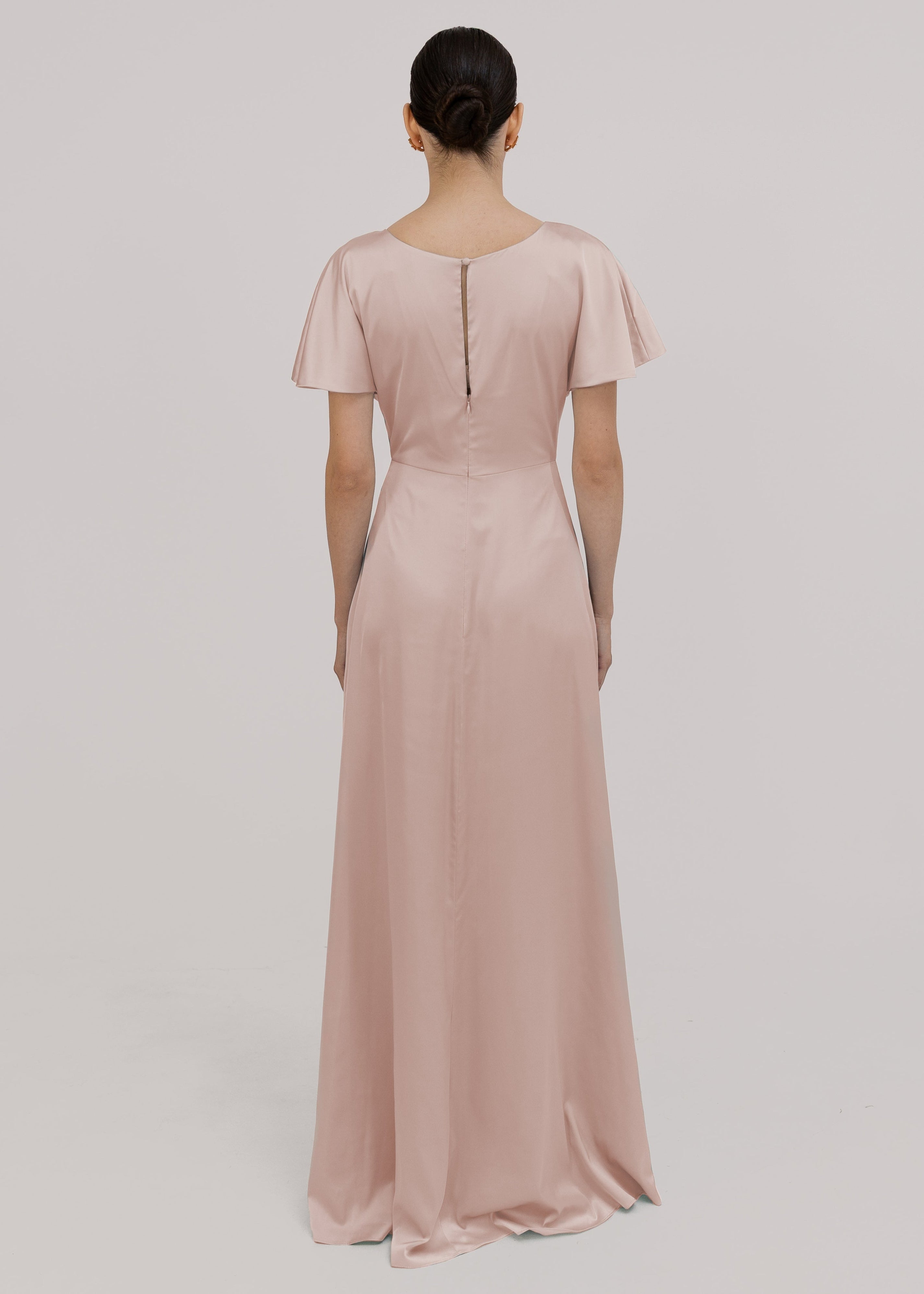 Model wears a blush pink satin bridesmaid dress with keyhole back, flutter sleeves on a white background by TH&TH Bridesmaids. 
