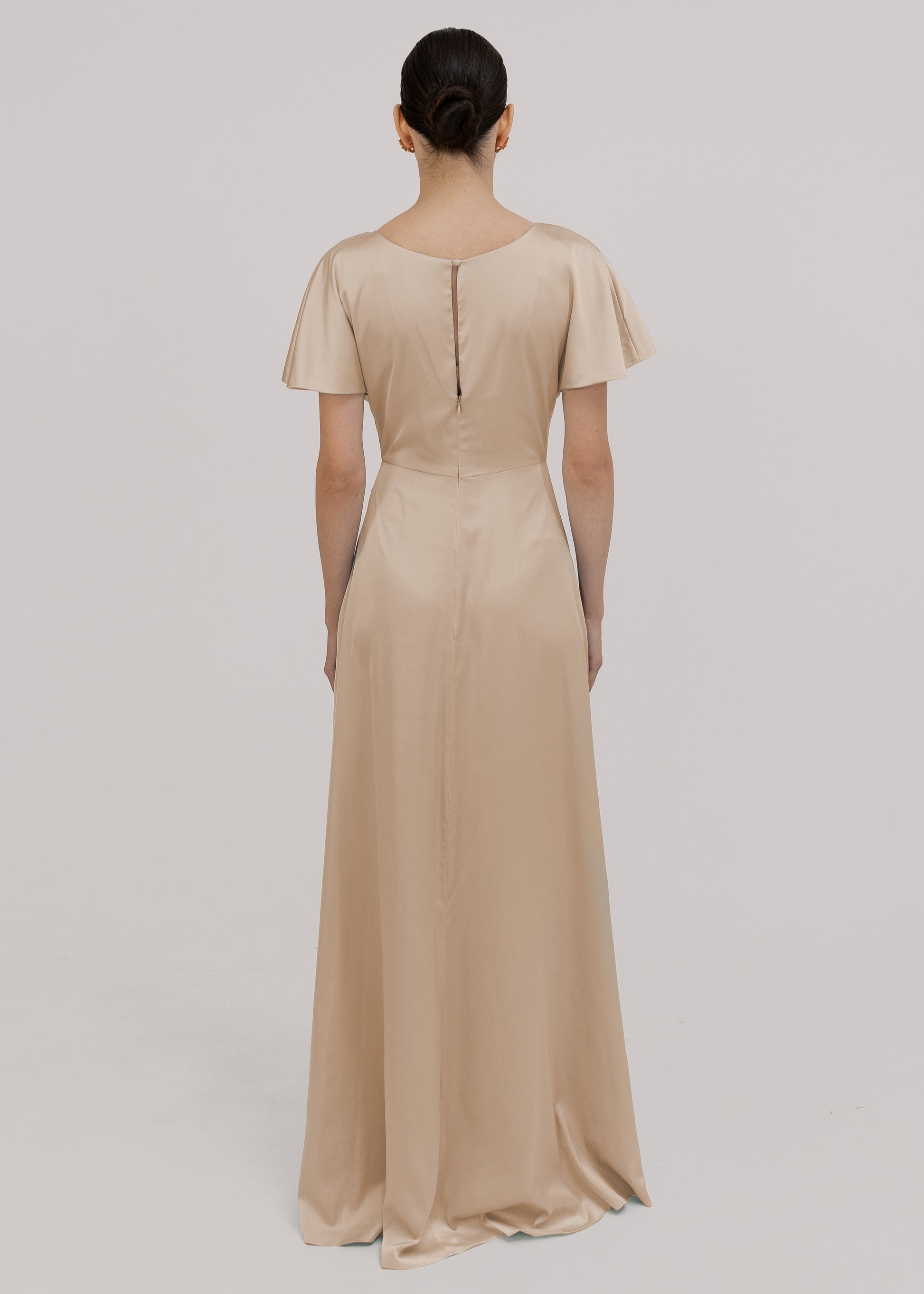 Model wears a champagne satin bridesmaid dress with flutter sleeves on a white background by TH&TH Bridesmaids. 
