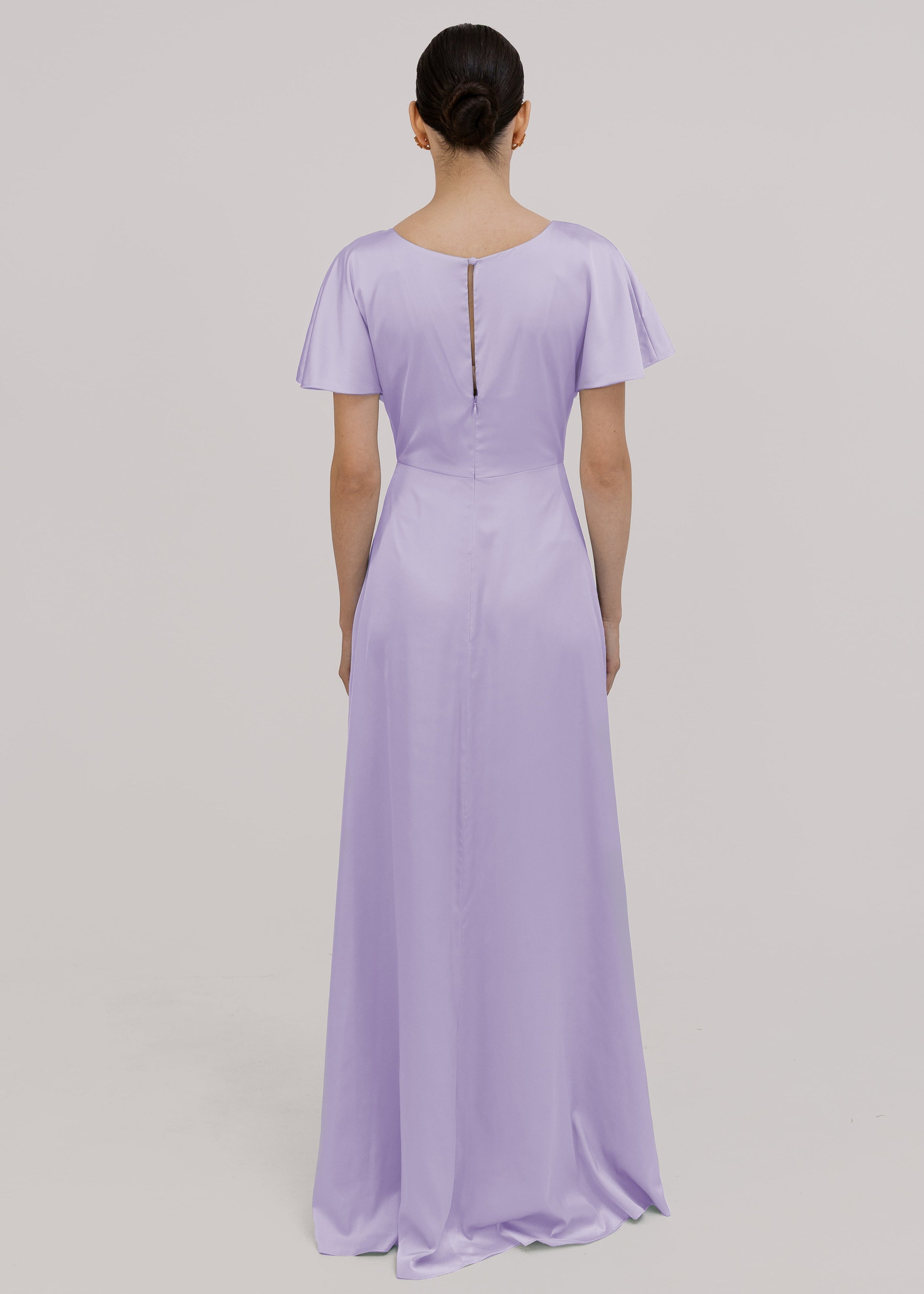 A woman wearing a lilac satin bridesmaid dress with flutter sleeves on a white background by TH&TH Bridesmaids. 
