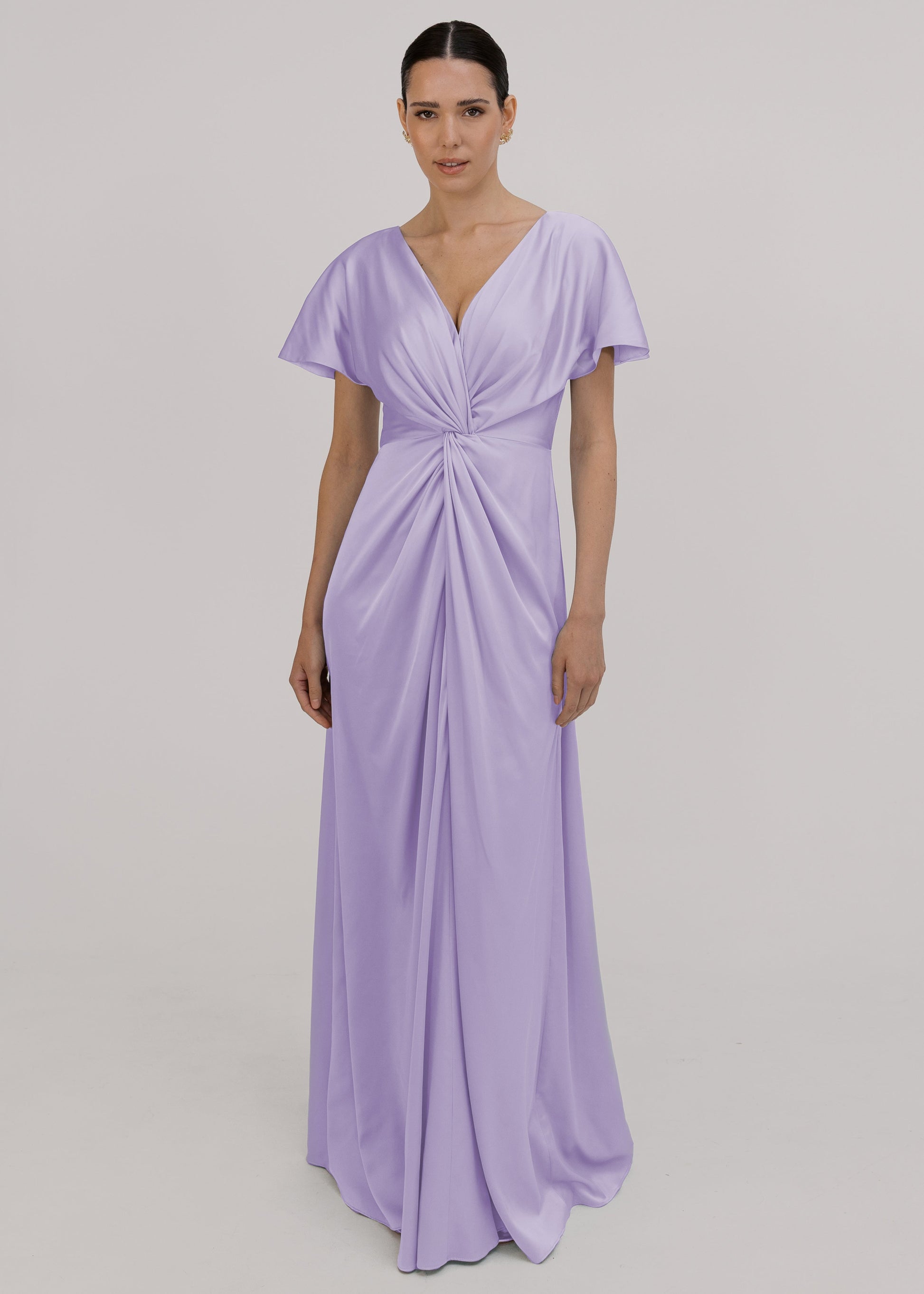 A woman wearing a lilac satin bridesmaid dress with v twist front neckline, flutter sleeves on a white background by TH&TH Bridesmaids. 
