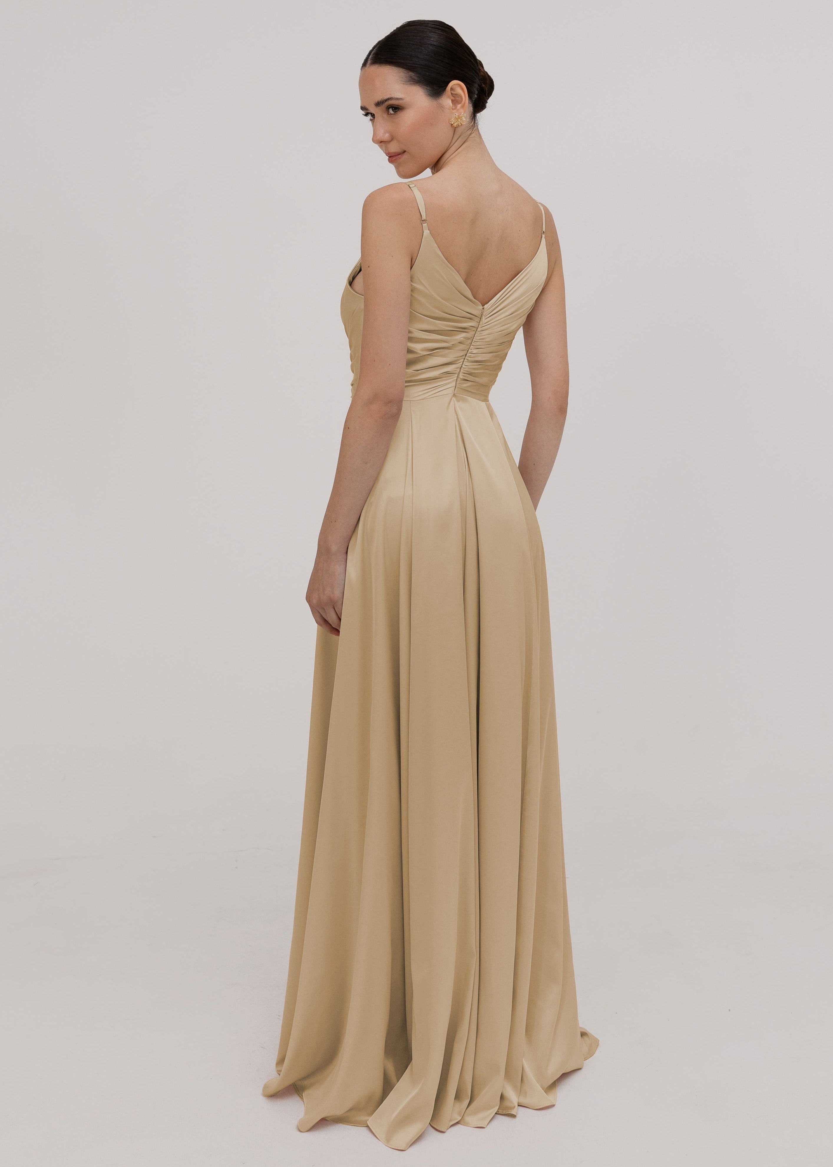 Model wearing a floor length champagne satin bridesmaid dress with V back and spaghetti straps by TH&TH Bridesmaids on a white background.