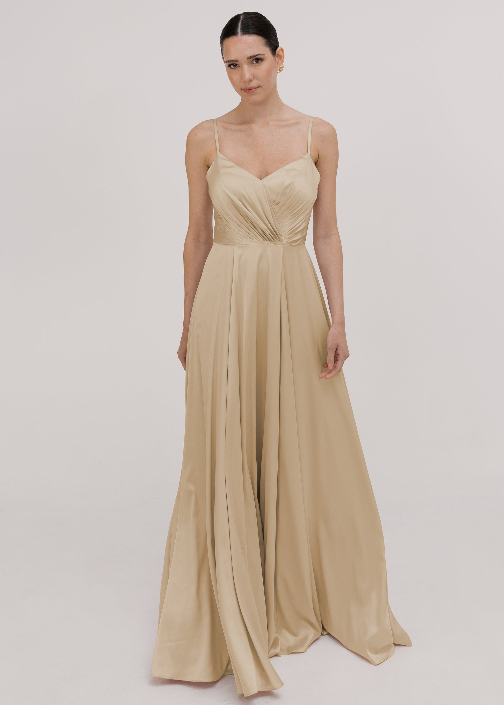 Model wearing a floor length champagne satin bridesmaid dress with V back and spaghetti straps by TH&TH Bridesmaids.