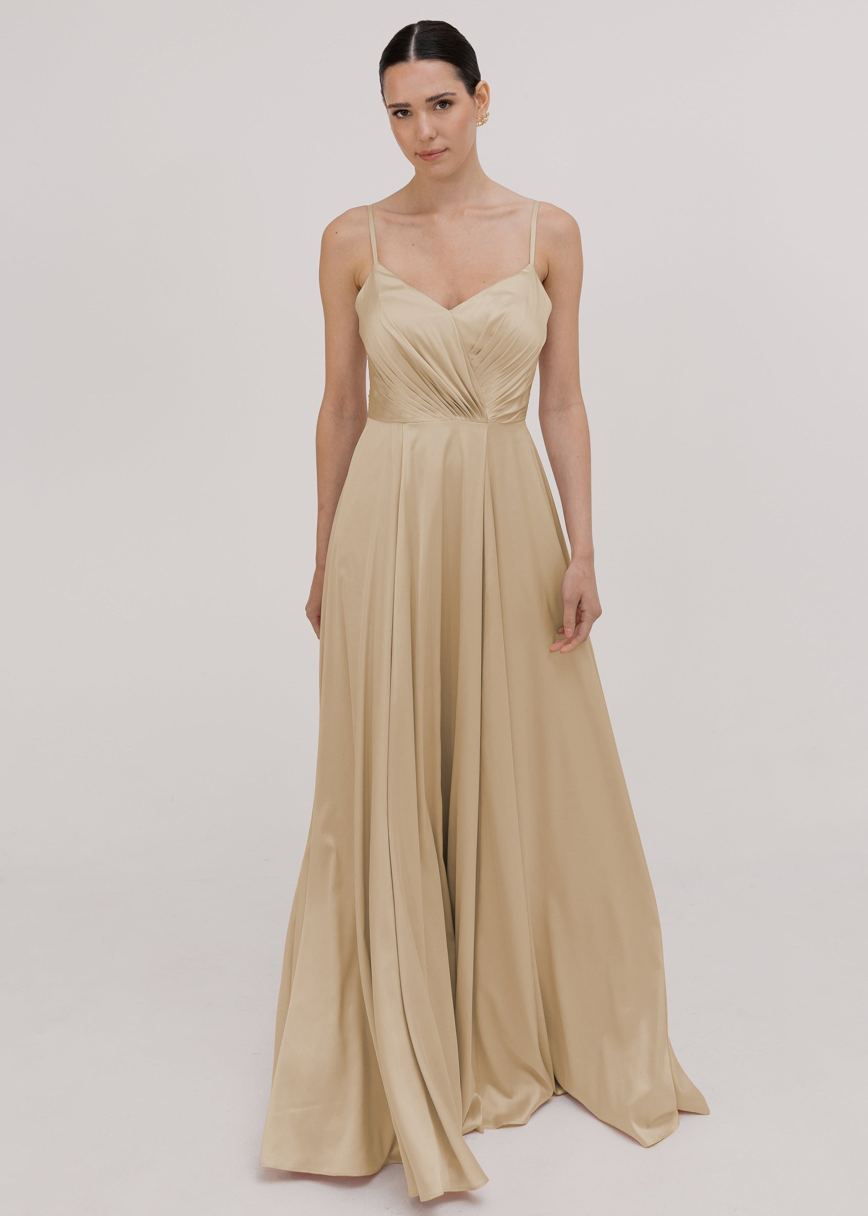 Model wearing a floor length champagne satin bridesmaid dress with V back and spaghetti straps by TH&TH Bridesmaids.