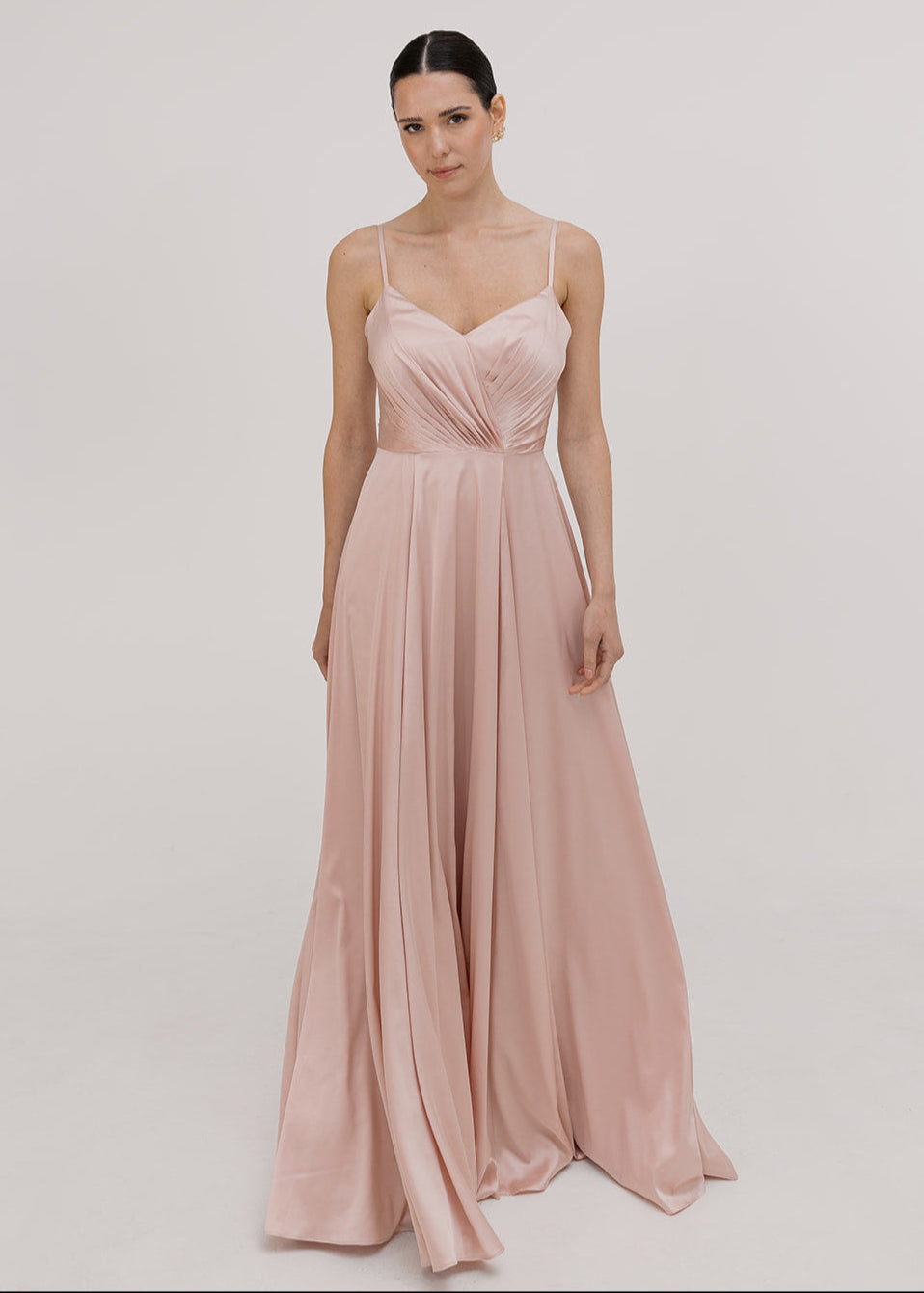 Model wearing a floor length blush pink satin bridesmaid dress with V back and spaghetti straps by TH&TH Bridesmaids.