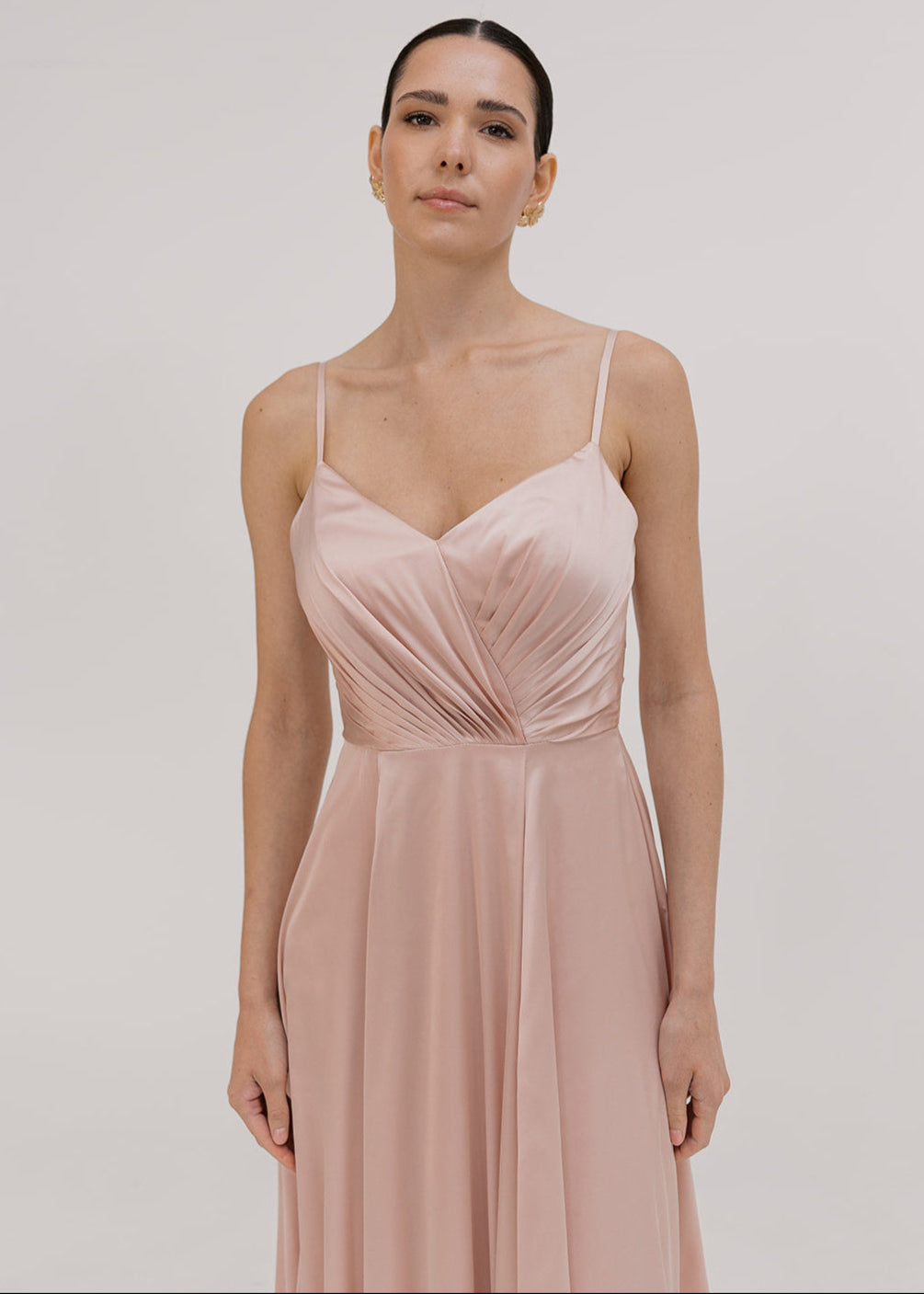 Model wearing a floor length blush pink satin bridesmaid dress with pleated bodice and spaghetti straps by TH&TH Bridesmaids.