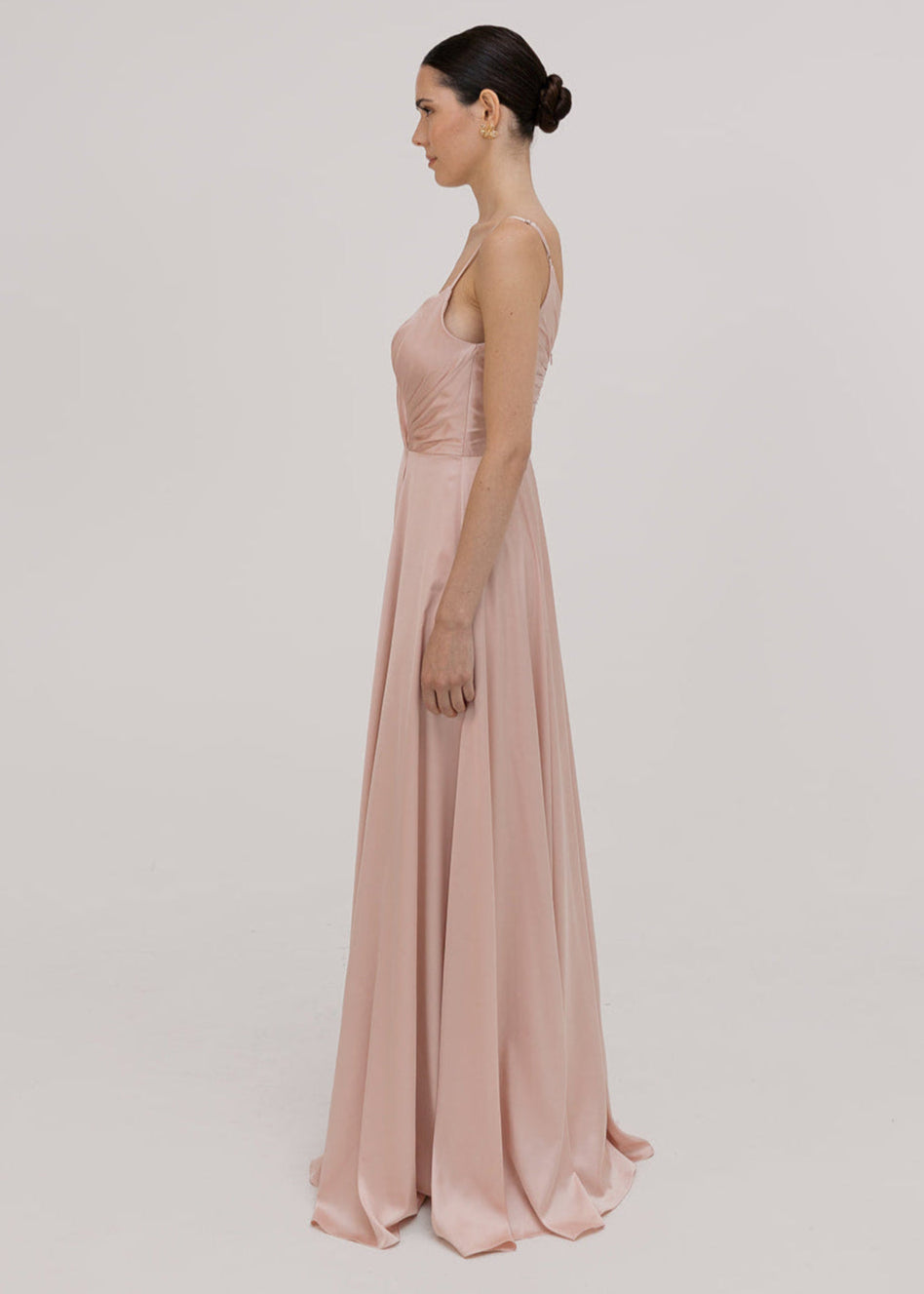 Model wearing a floor length blush pink satin bridesmaid dress with V back and spaghetti straps by TH&TH Bridesmaids.
