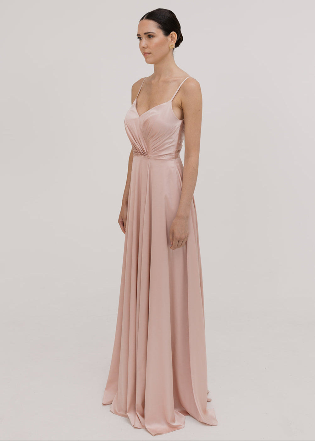 Model wearing a floor length blush pink satin bridesmaid dress with V back and spaghetti straps by TH&TH Bridesmaids.
