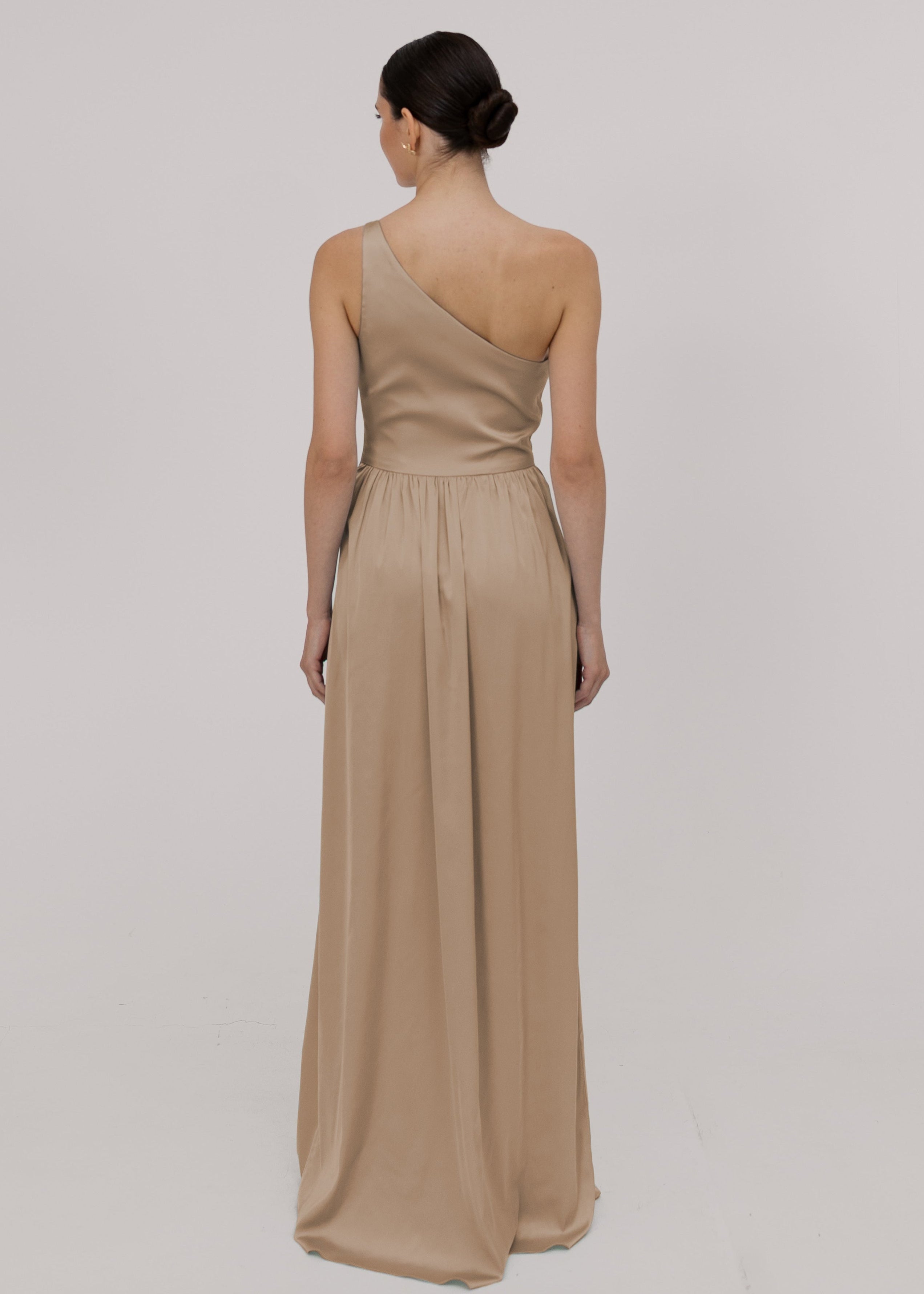 Model wearing a floor length champagne satin bridesmaid dress with one shoulder and gathered skirt by TH&TH Bridesmaids.
