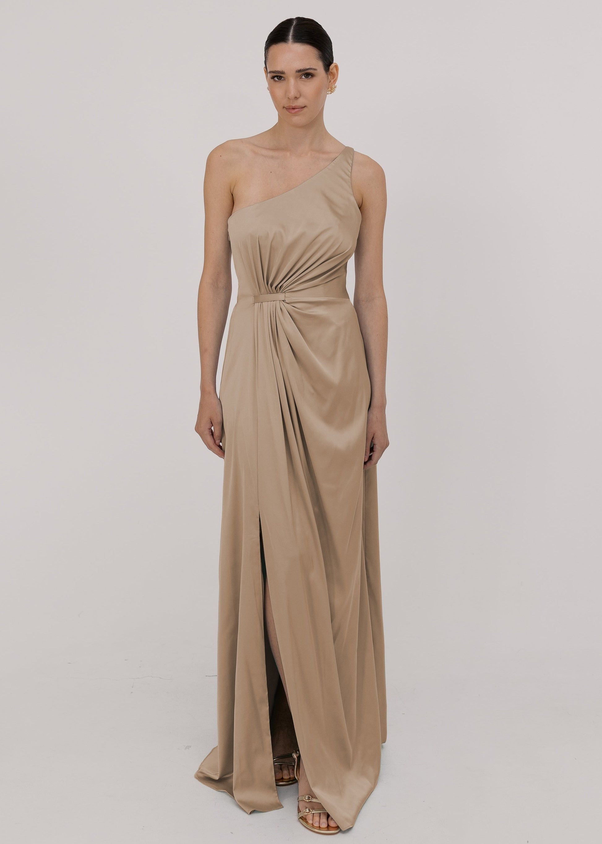 Model wearing a floor length champagne satin bridesmaid dress with one shoulder and slit in skirt by TH&TH Bridesmaids.
