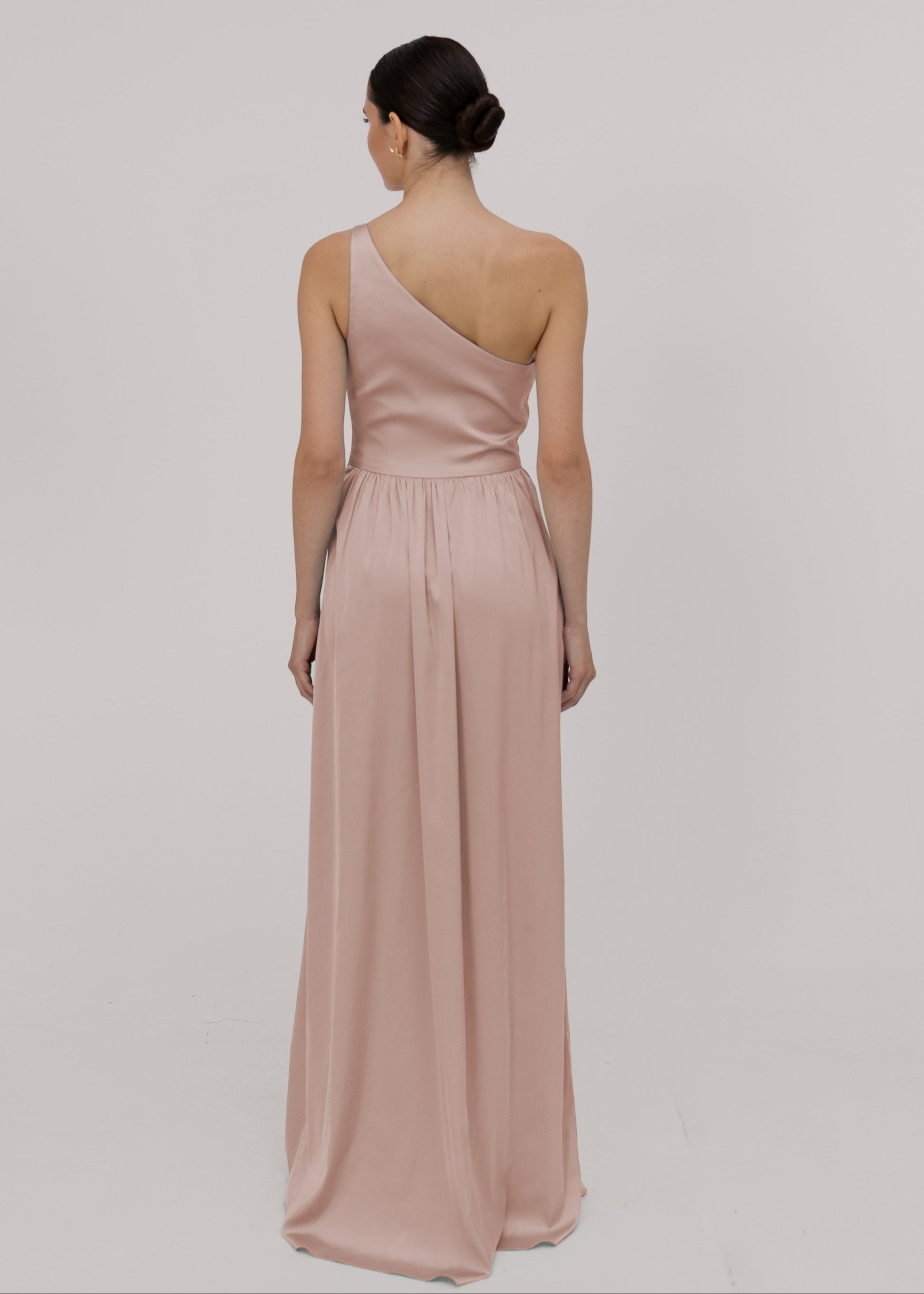 Model wearing a floor length blush pink satin bridesmaid dress with one shoulder back view TH&TH Bridesmaids.
