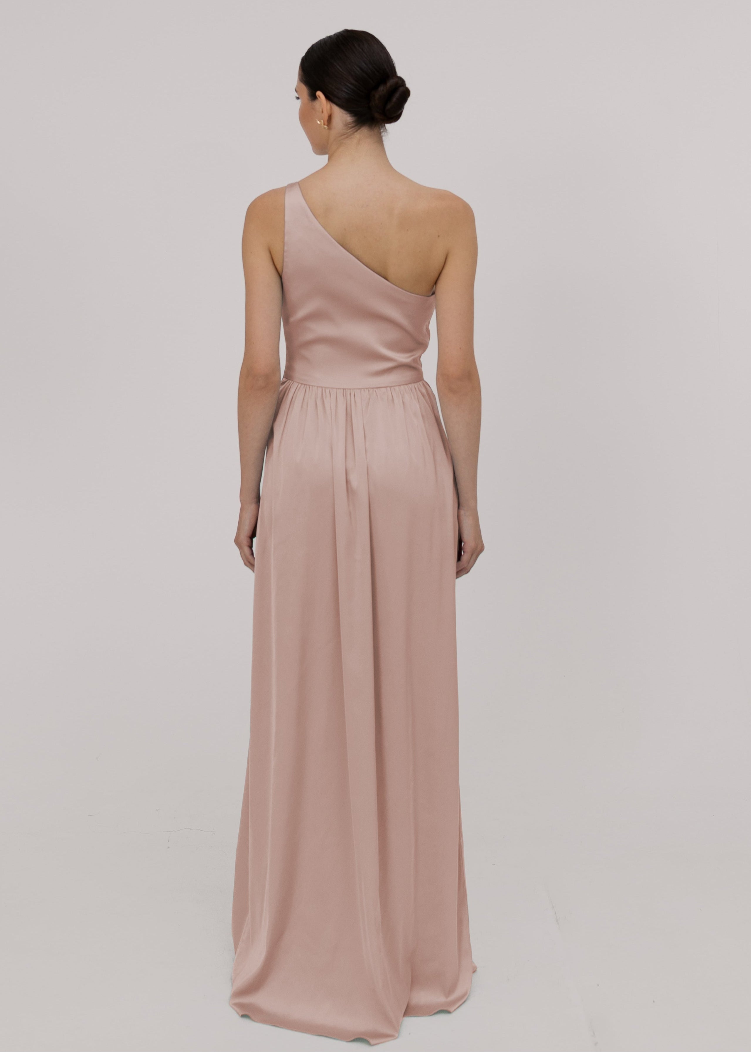 Model wearing a floor length blush pink satin bridesmaid dress with one shoulder back view TH&TH Bridesmaids.