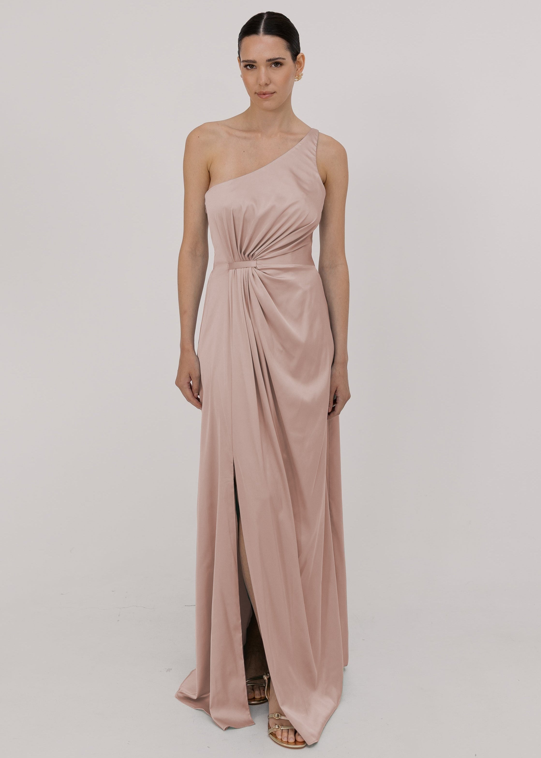Model wearing a floor length blush pink satin bridesmaid dress with one shoulder and slit in skirt by TH&TH Bridesmaids.