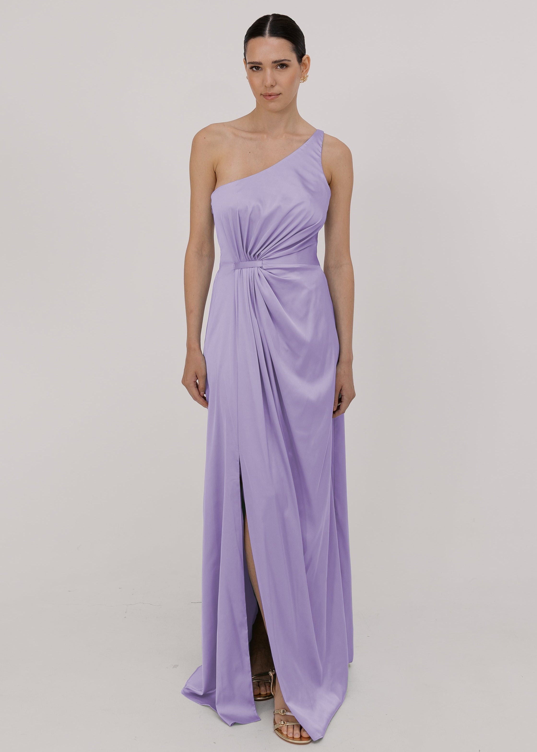 Model wearing a floor length lilac satin bridesmaid dress with one shoulder and slit in skirt by TH&TH Bridesmaids.
