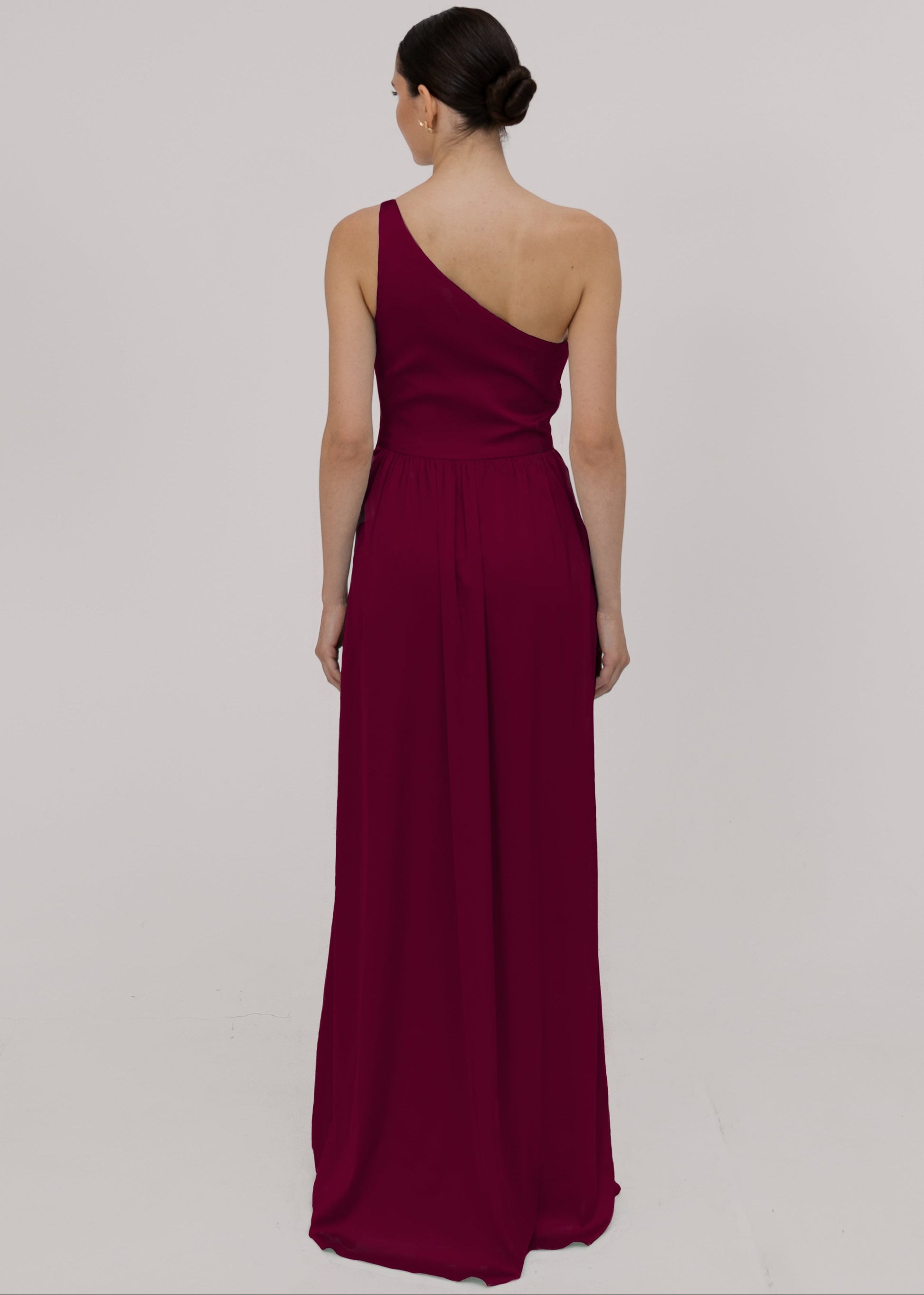 Model wearing a floor length burgundy satin bridesmaid dress with one shoulder and slit in skirt by TH&TH Bridesmaids.