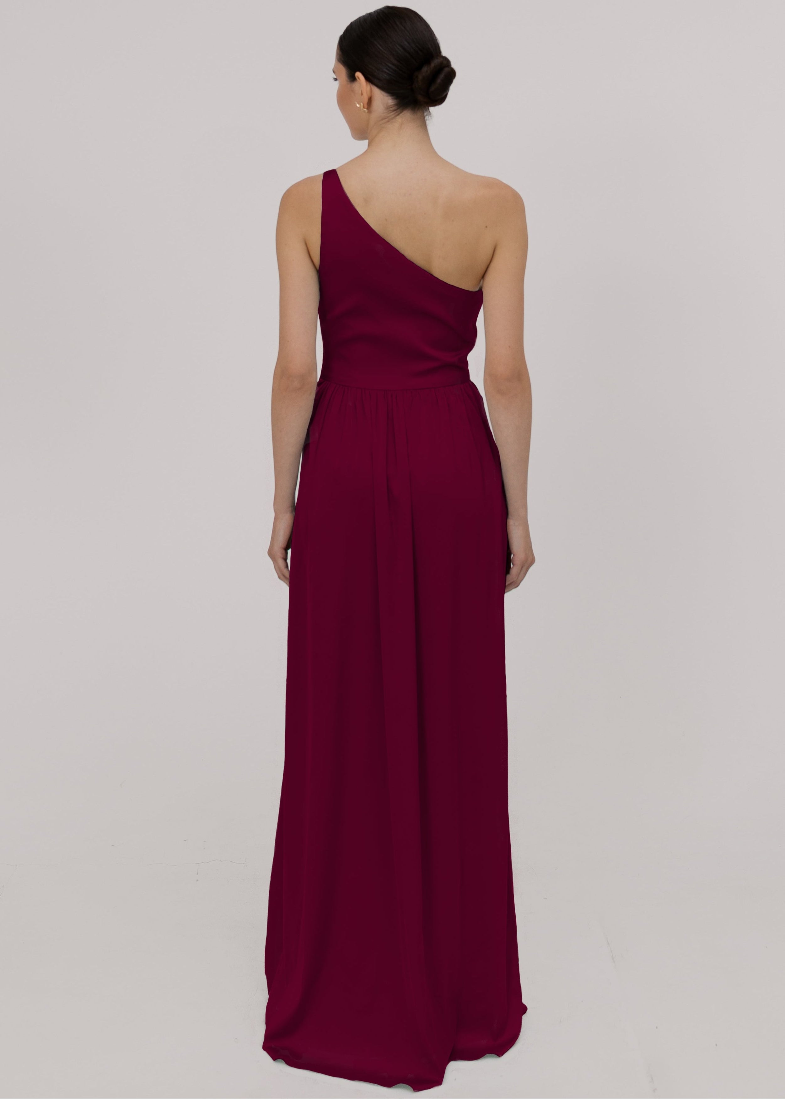 Model wearing a floor length burgundy satin bridesmaid dress with one shoulder and slit in skirt by TH&TH Bridesmaids.