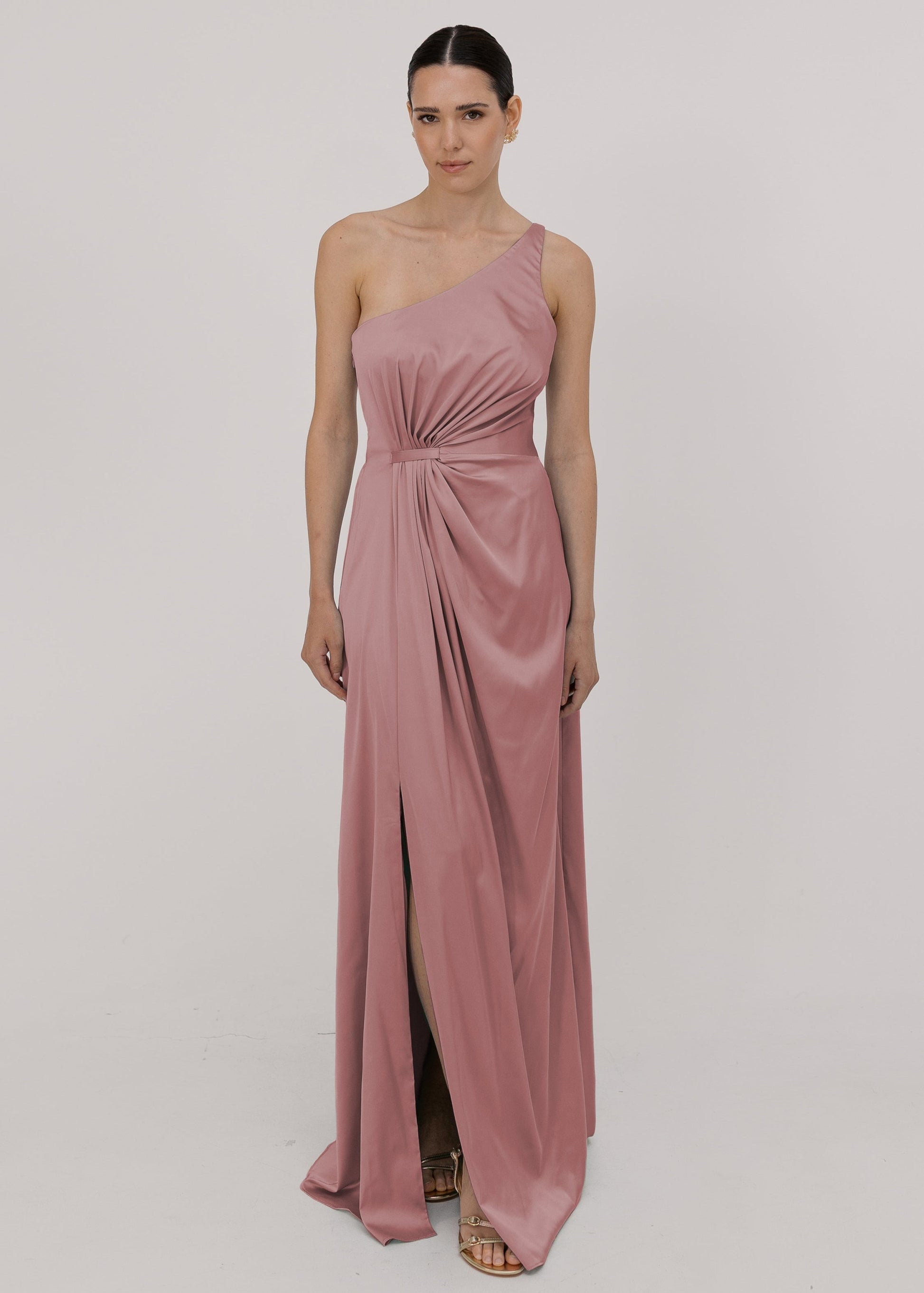 Model wearing a floor length pink satin bridesmaid dress with one shoulder and slit in skirt by TH&TH Bridesmaids.
