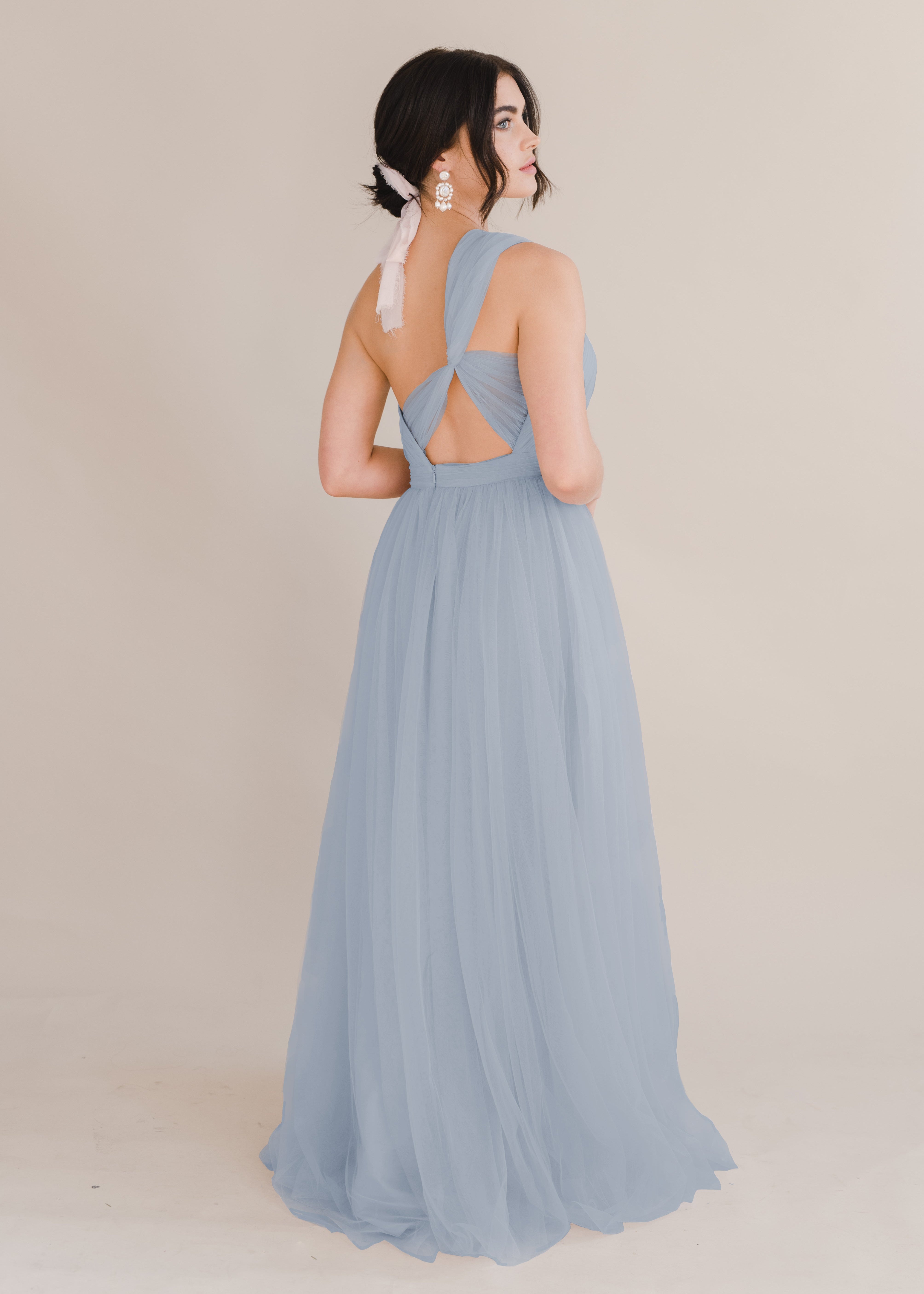 A woman wearing a dusty blue bridesmaid dress with one shoulder strap on a white background by TH&TH Bridesmaids. 
