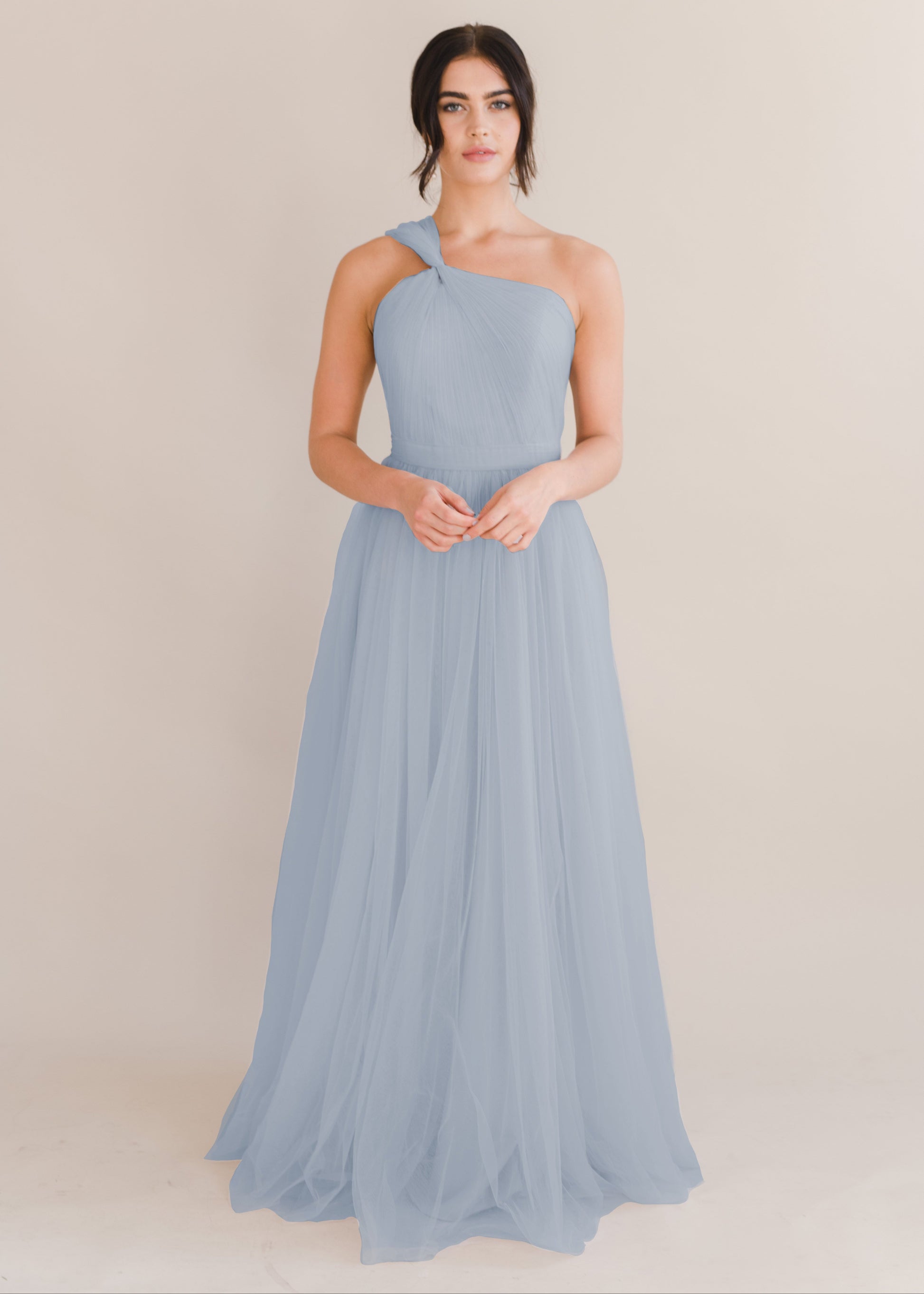 A woman wearing a dusty blue bridesmaid dress with one shoulder strap on a white background by TH&TH Bridesmaids. 
