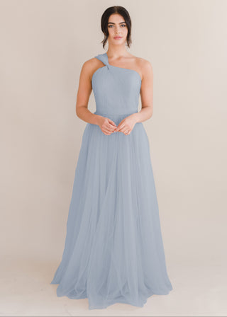 A woman wearing a dusty blue bridesmaid dress with one shoulder strap on a white background by TH&TH Bridesmaids. 

