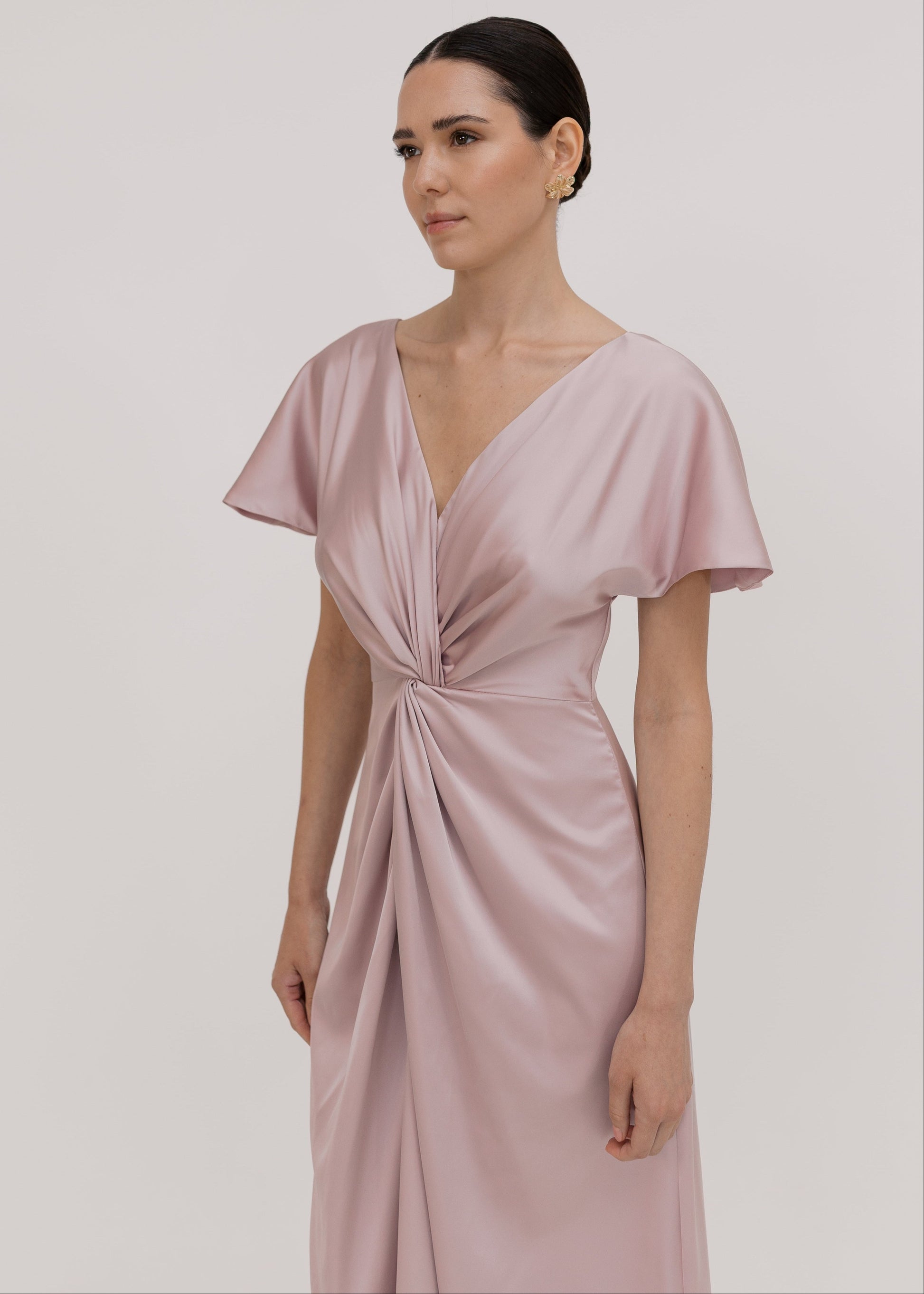 Woman wearing a long smoked blush pink bridesmaid dress with sleeves, bra friendly high back and twist knot detail in satin.