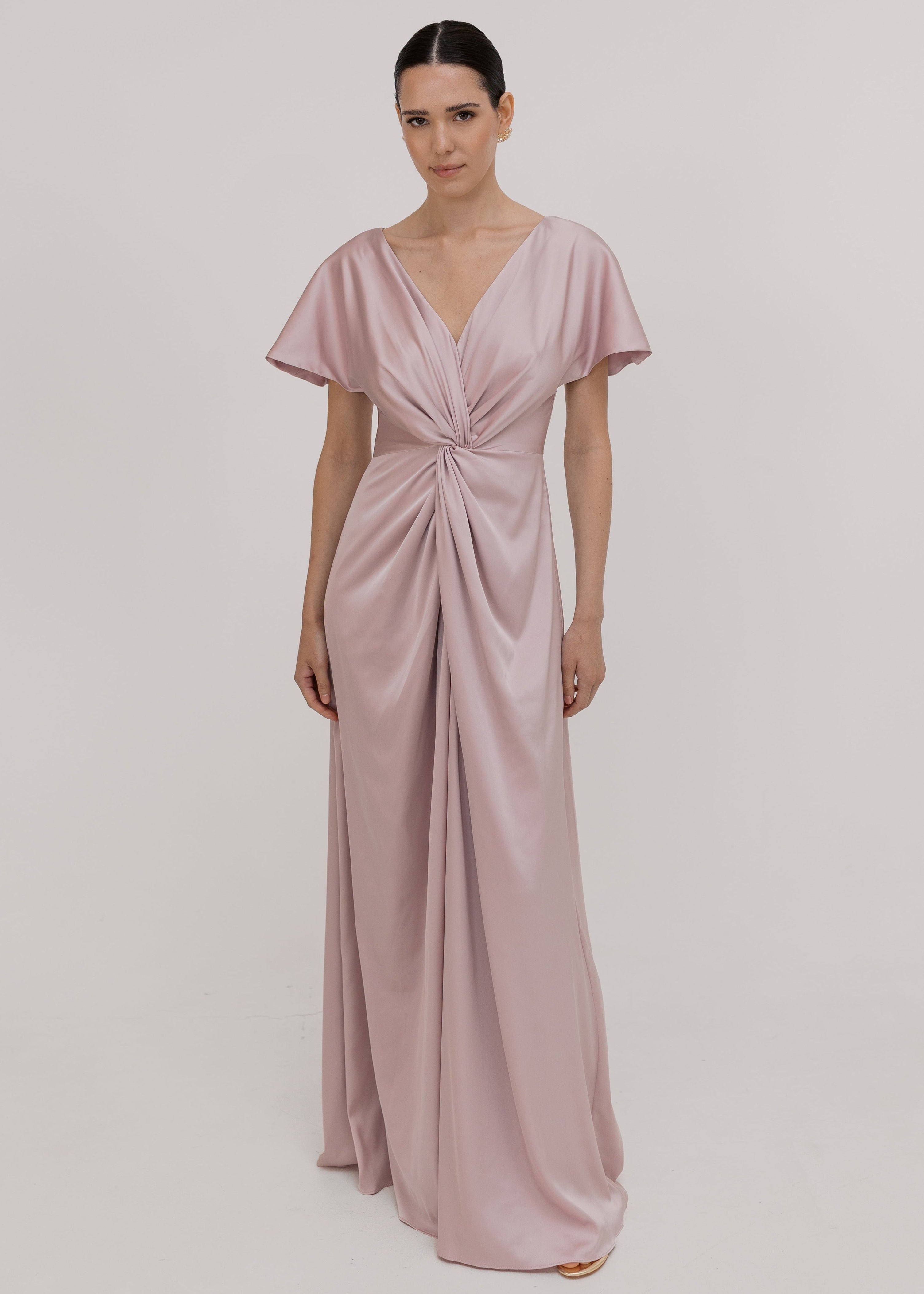 Woman wearing a long smoked blush pink bridesmaid dress with sleeves, bra friendly high back and twist knot detail in satin.