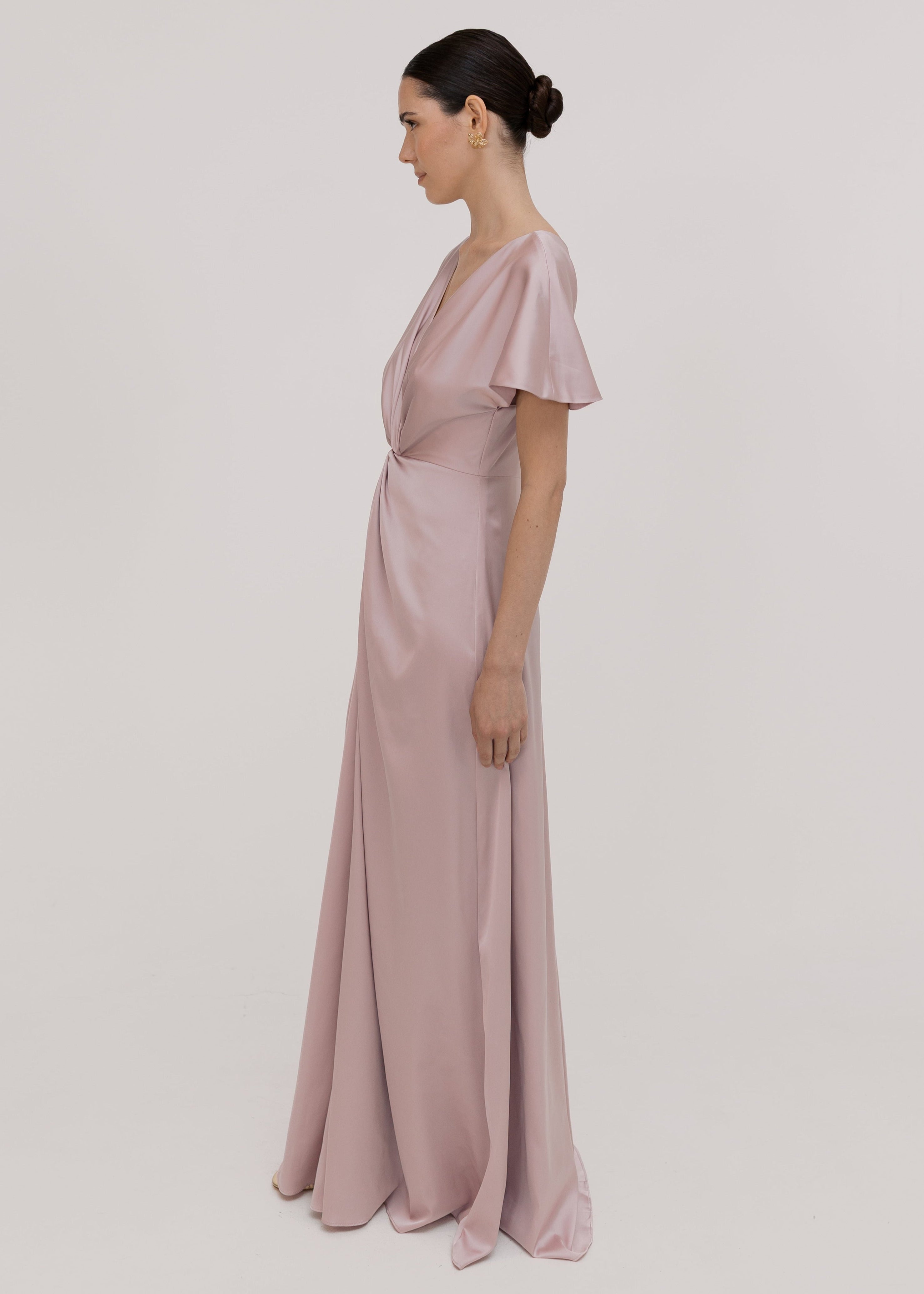 Woman wearing a long smoked blush pink bridesmaid dress with sleeves, bra friendly high back and twist knot detail in satin.