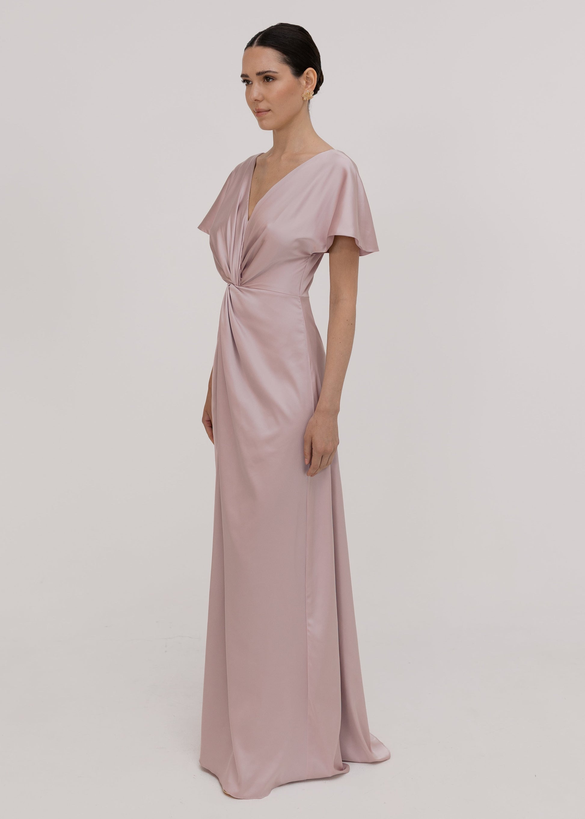 Woman wearing a long smoked blush pink bridesmaid dress with sleeves, bra friendly high back and twist knot detail in satin.