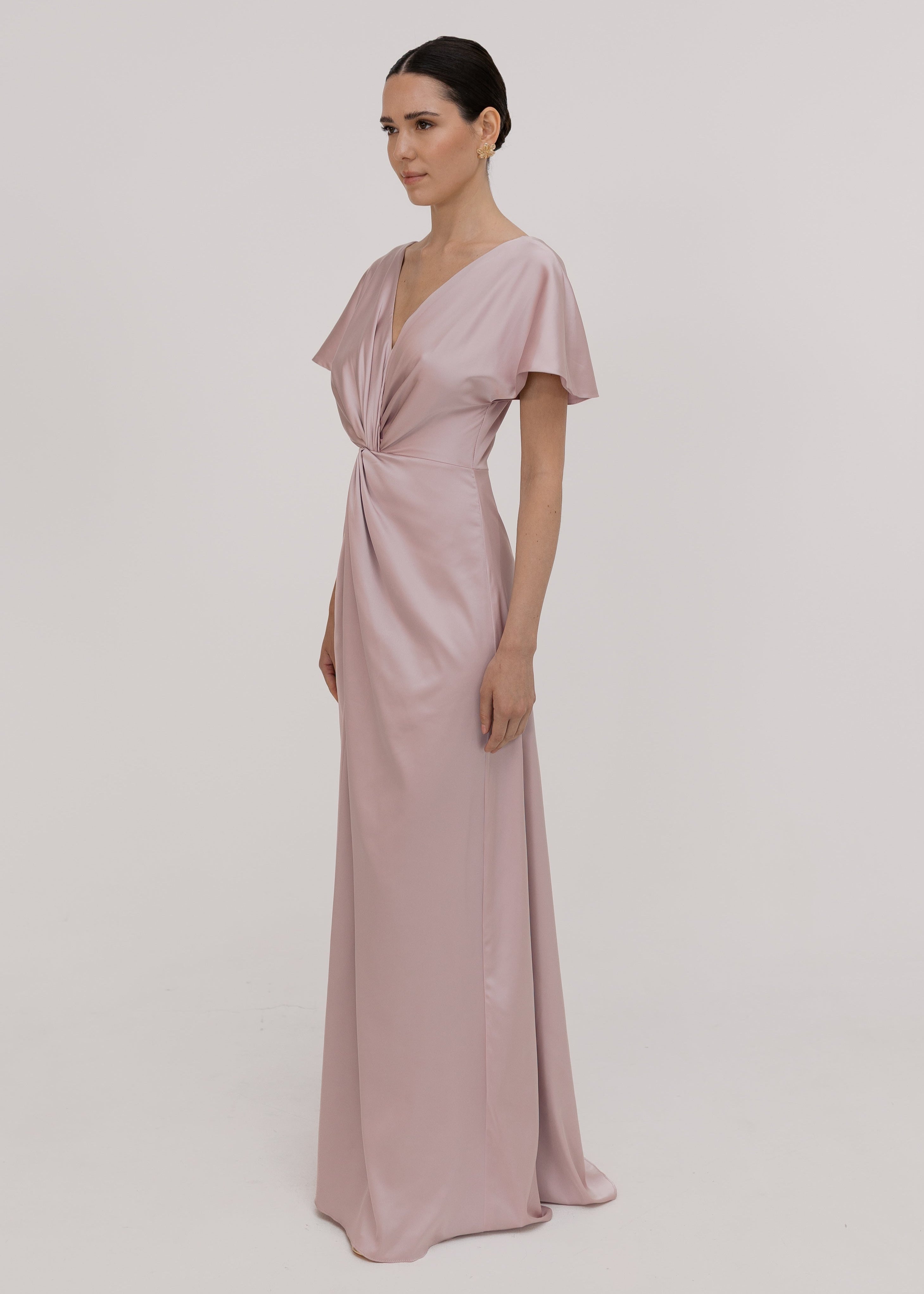 Woman wearing a long smoked blush pink bridesmaid dress with sleeves, bra friendly high back and twist knot detail in satin.