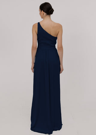 Woman wearing a long navy bridesmaid dress with one shoulder and cinched waist detail in satin.