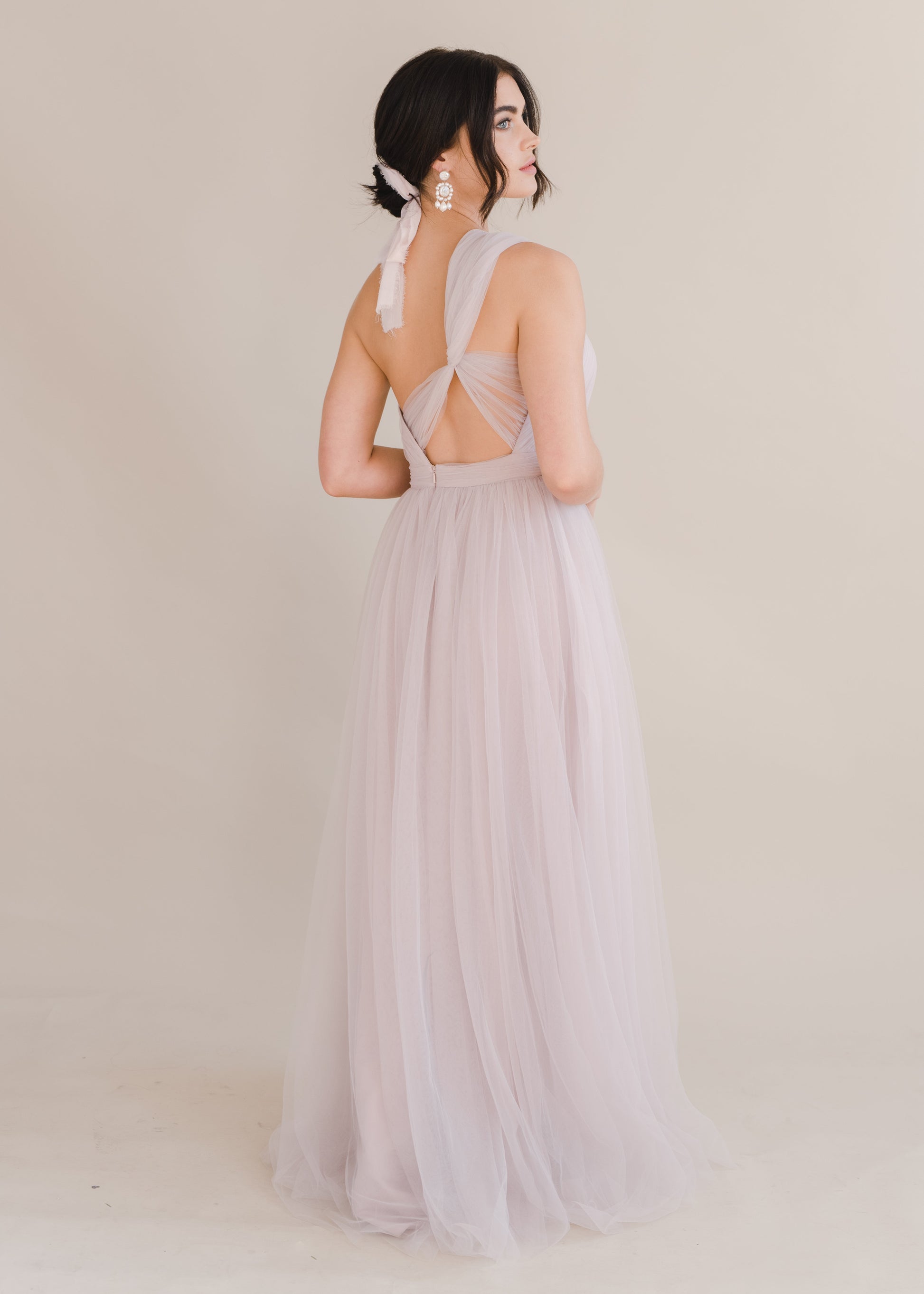 Woman wearing a long smoked blush pink bridesmaid dress with one shoulder and full skirt in tulle.