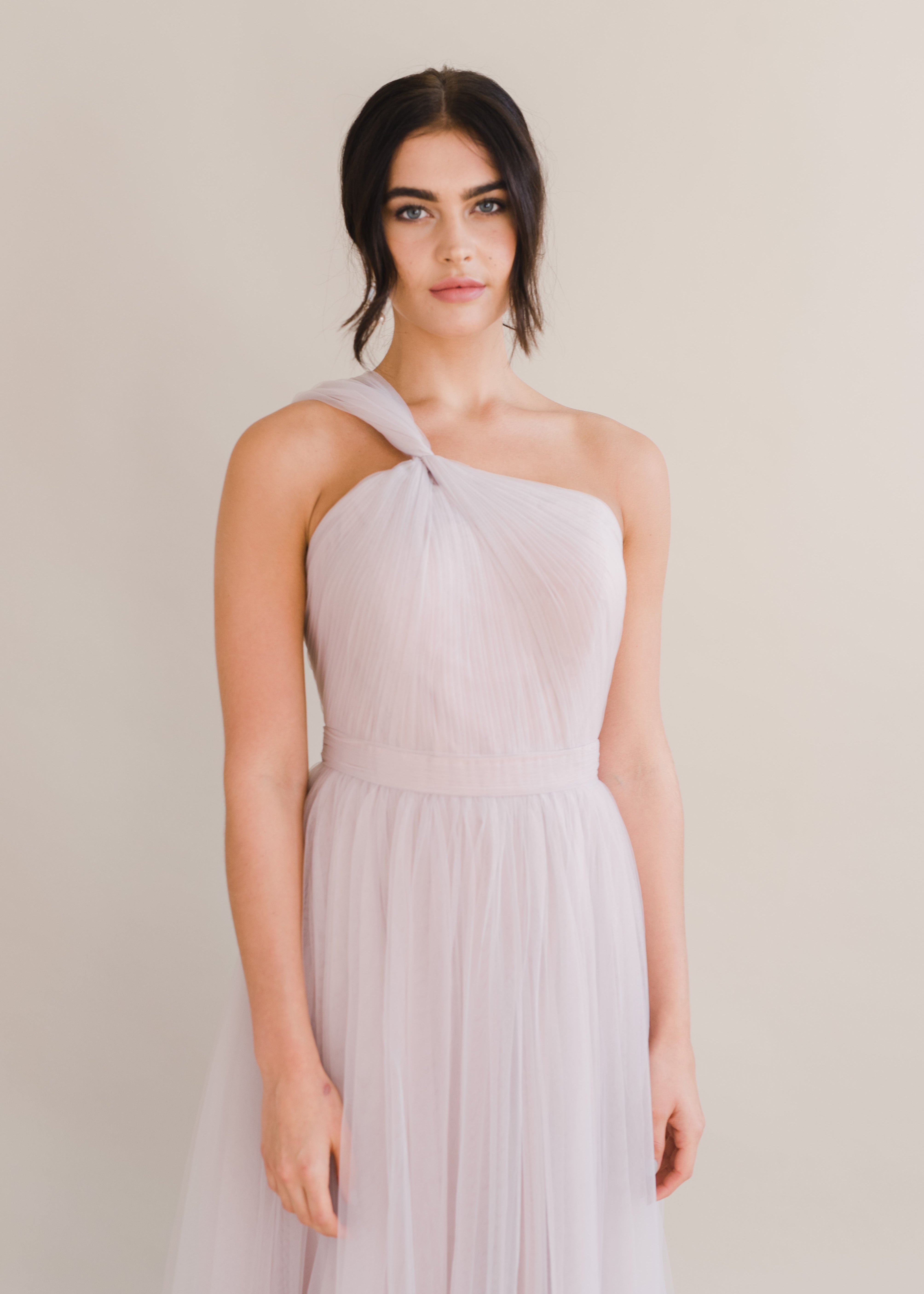Woman wearing a long smoked blush pink bridesmaid dress with one shoulder and full skirt in tulle.