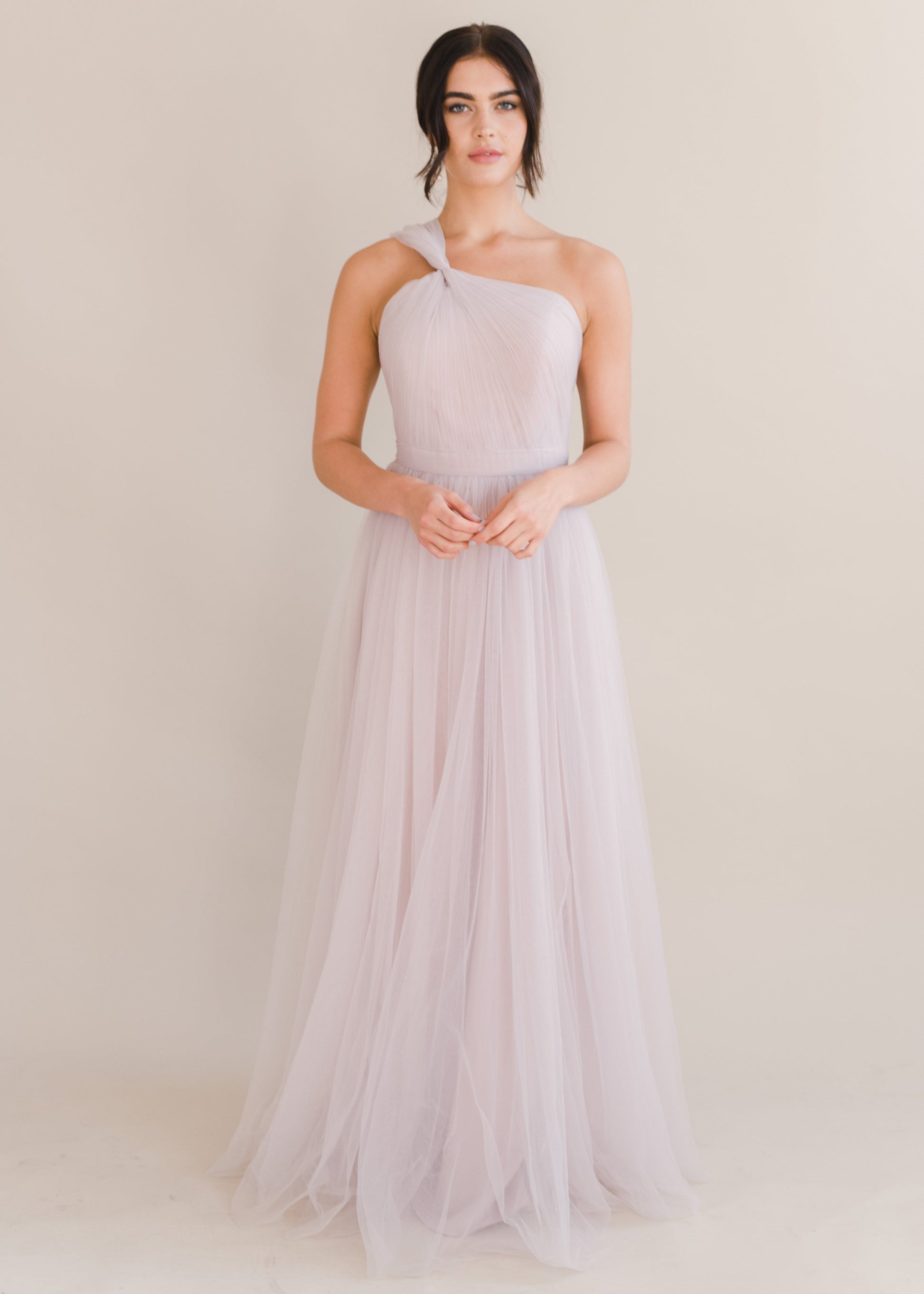 Woman wearing a long smoked blush pink bridesmaid dress with one shoulder and full skirt in tulle.