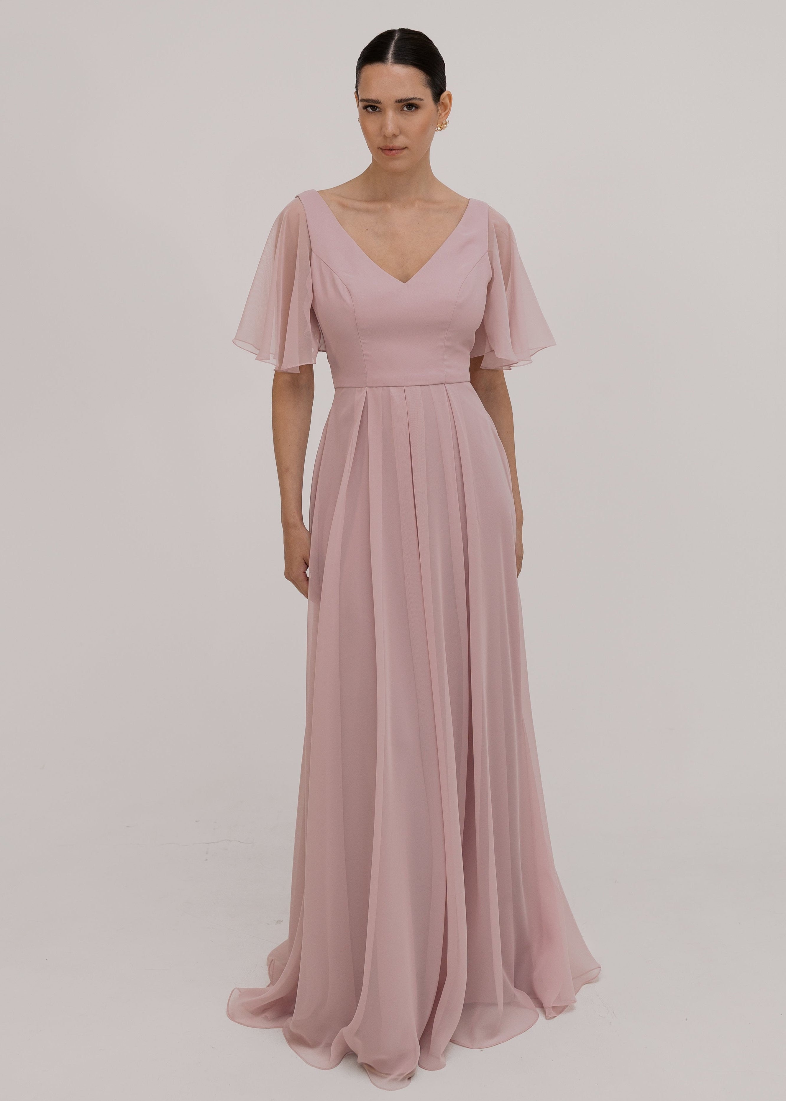 Woman wearing a long smoked blush pink bridesmaid dress with V neck and full skirt in chiffon.