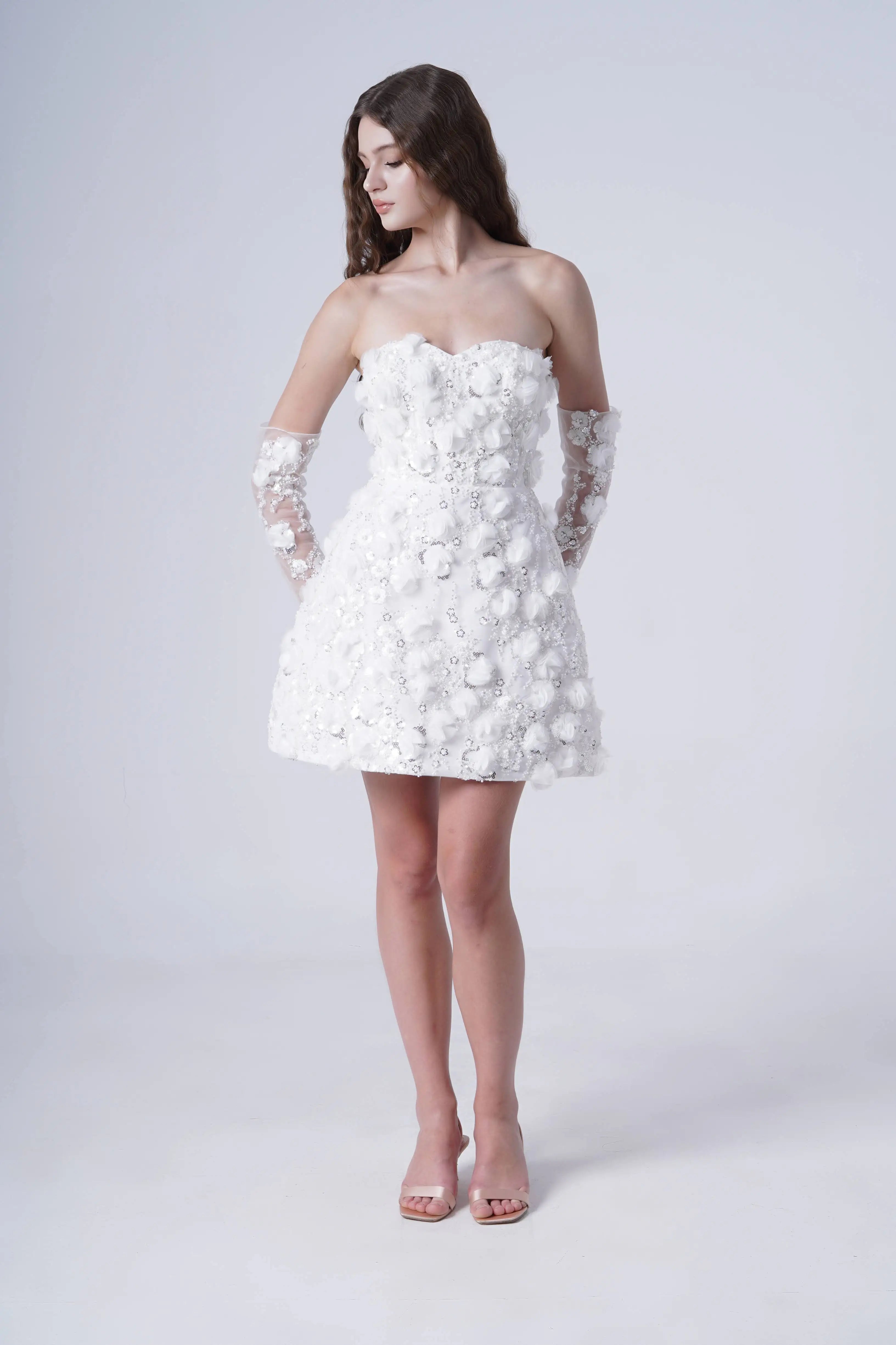 Woman wearing a white strapless dress with floral details on a plain background