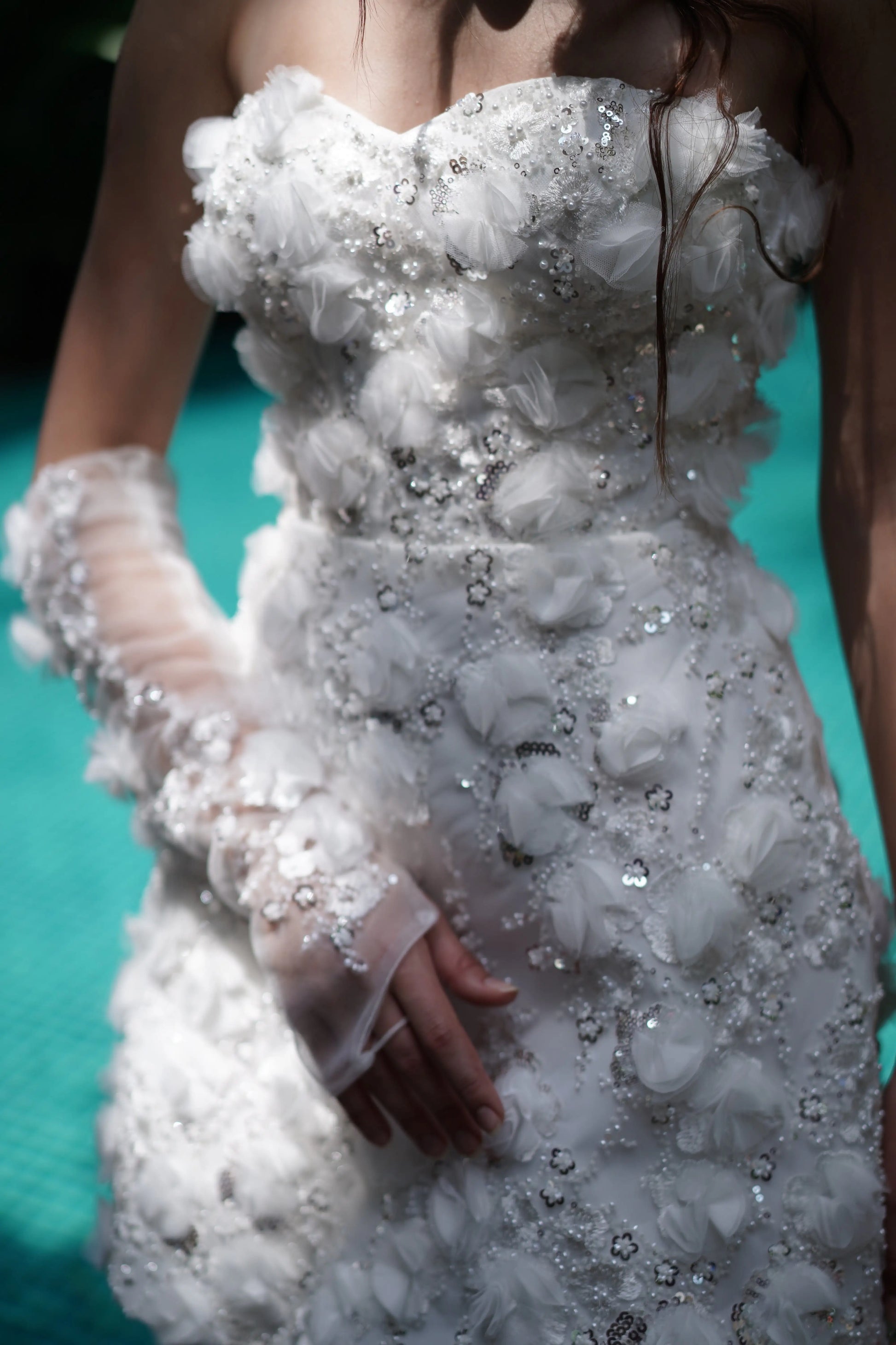 A close up of an embellished bridal mini dress with embellishments and embellished matching gloves by a pool.