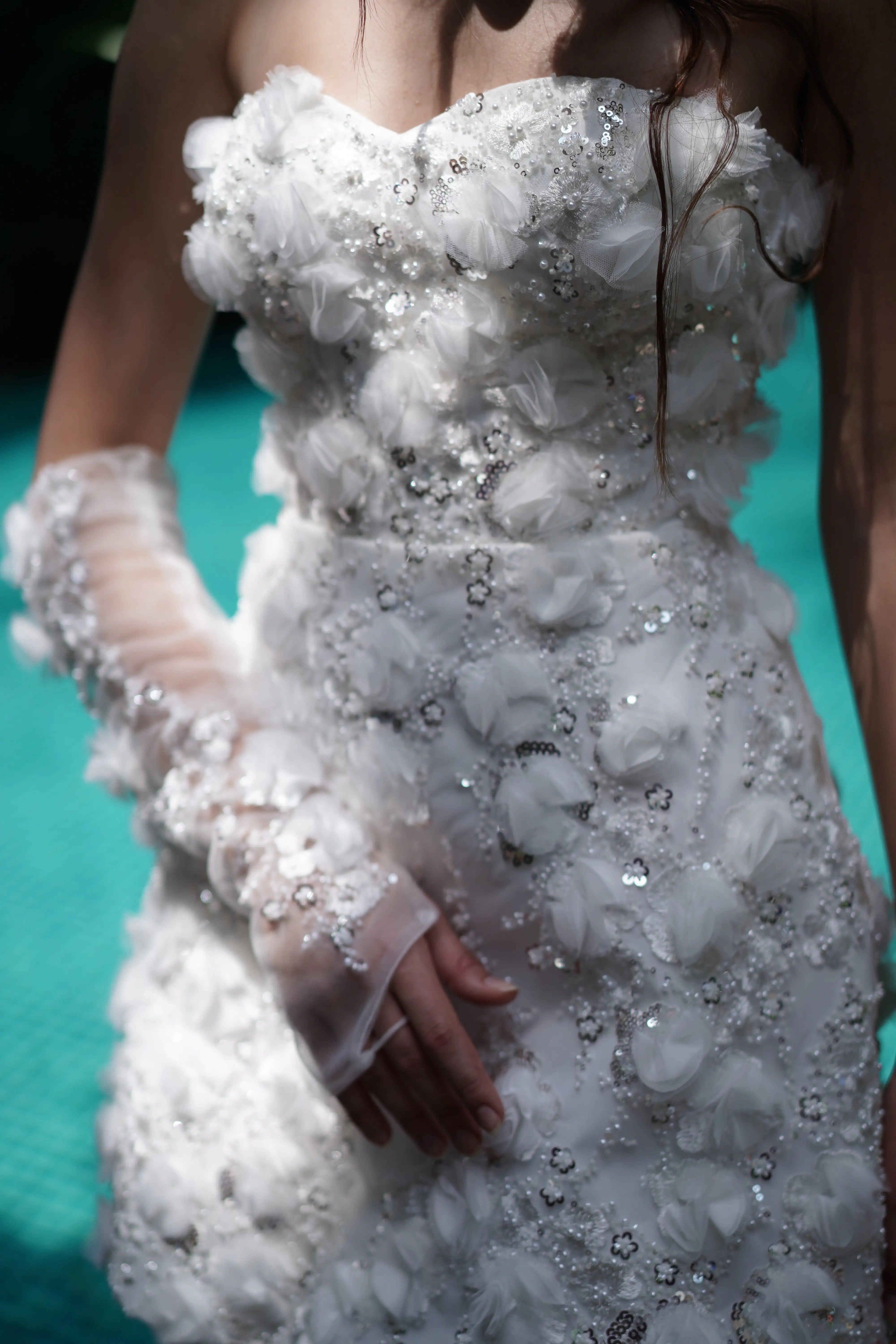 A close up of an embellished bridal mini dress with embellishments and embellished matching gloves by a pool.